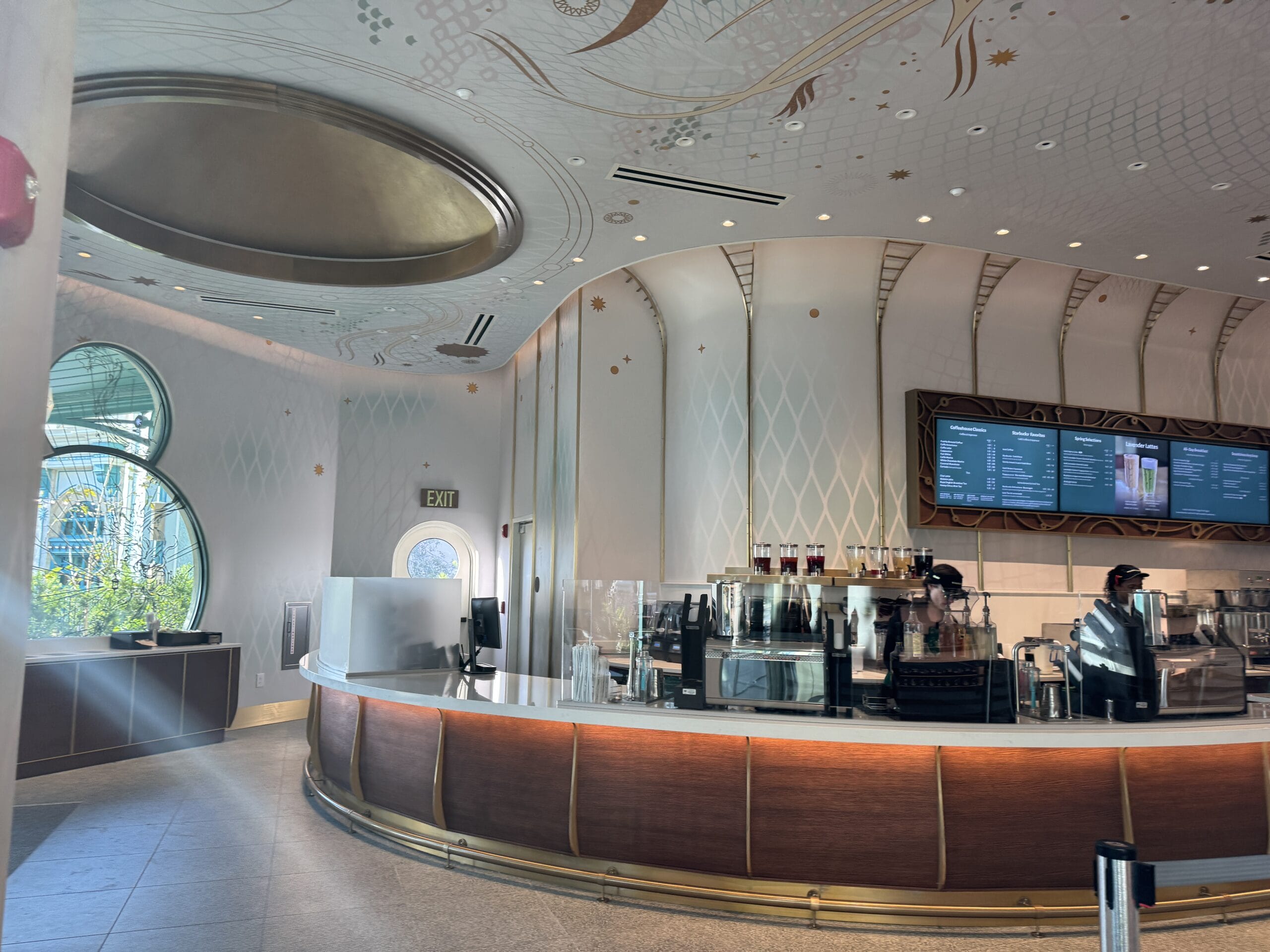 Chic coffee shop with a curved counter, digital menus, and baristas—reminiscent of Starbucks at Disney parks—under elegant ceiling.