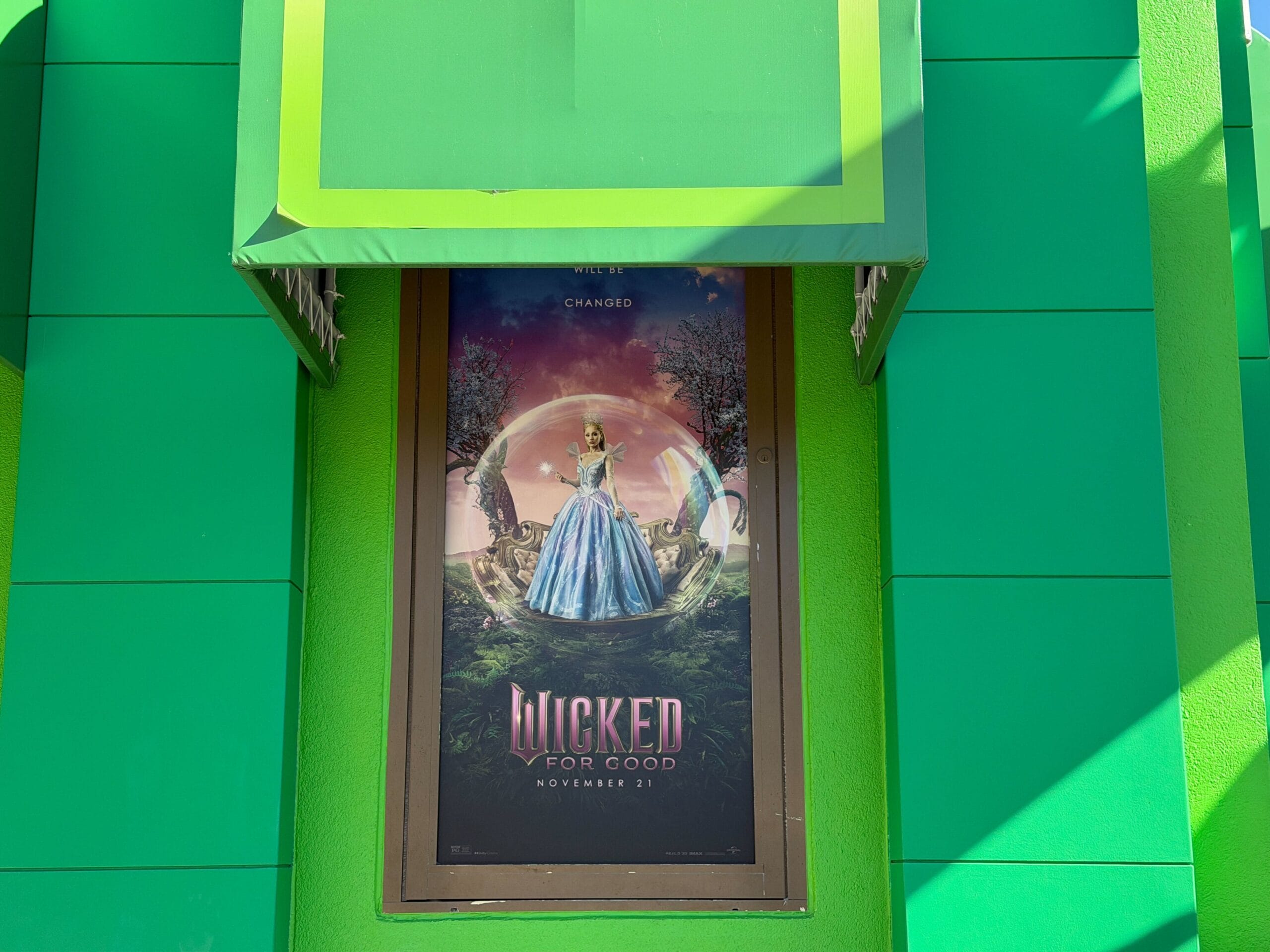 A "Wicked" movie poster shows iconic costumes and a woman in blue; the castle in back is not Cinderella Castle from Disney parks.