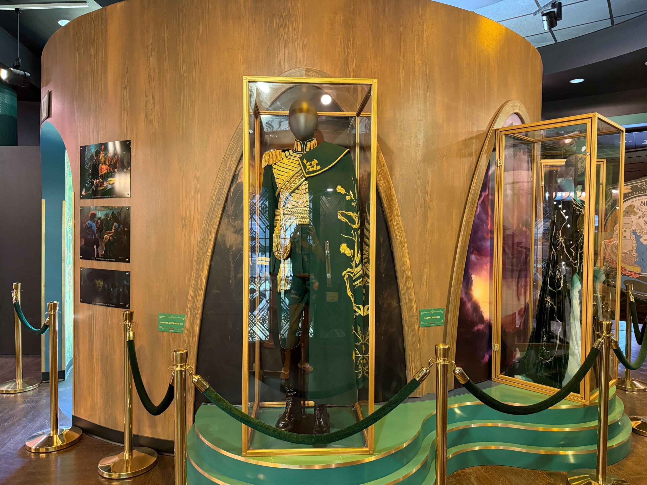 A Wicked costume with gold and green accents is displayed in a glass case, reminiscent of Broadway displays at Disney parks.
