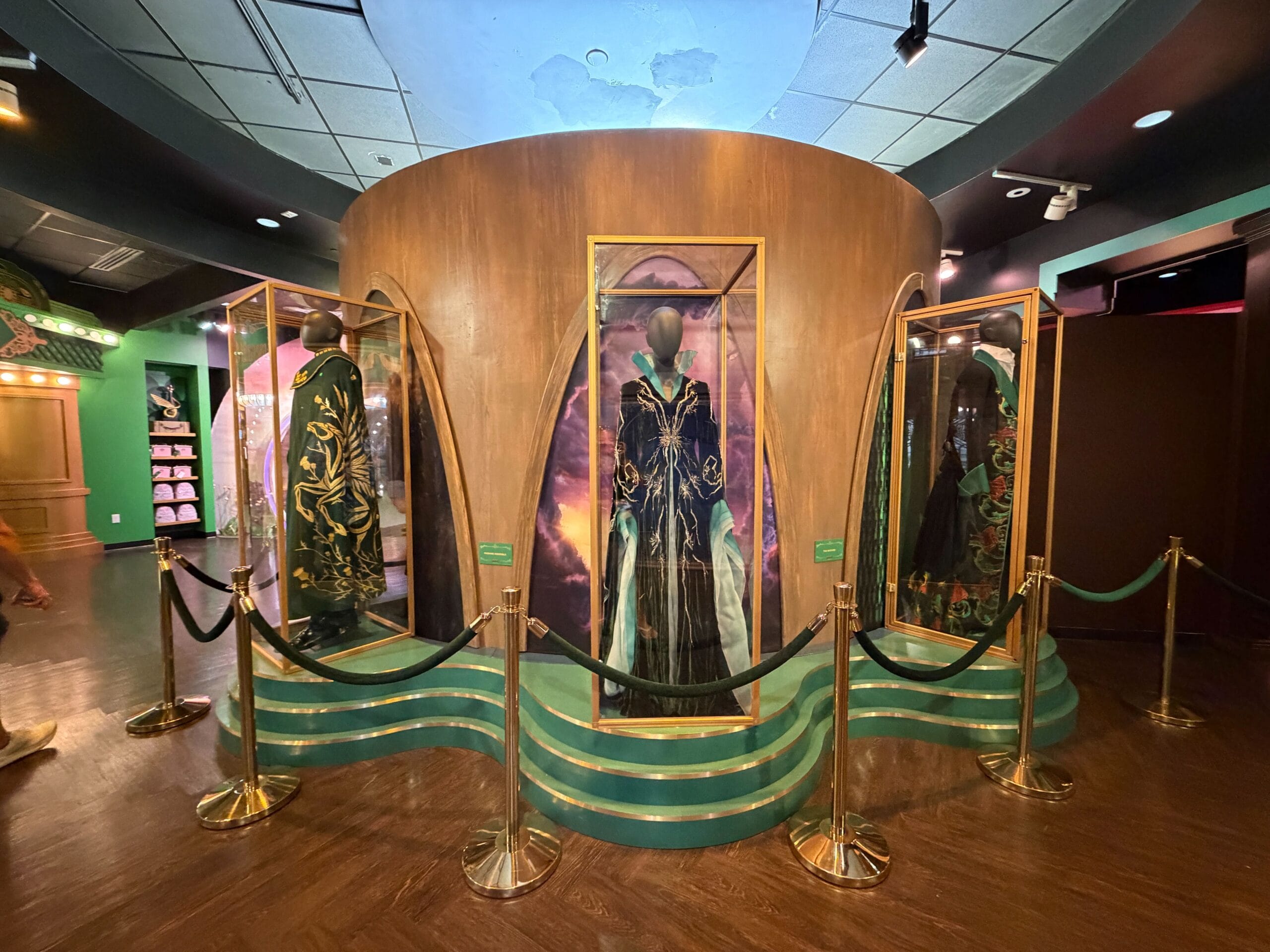 Three ornate Wicked costumes in glass cases highlight a Universal Studios exhibit, differing from Disney Park displays and castles.