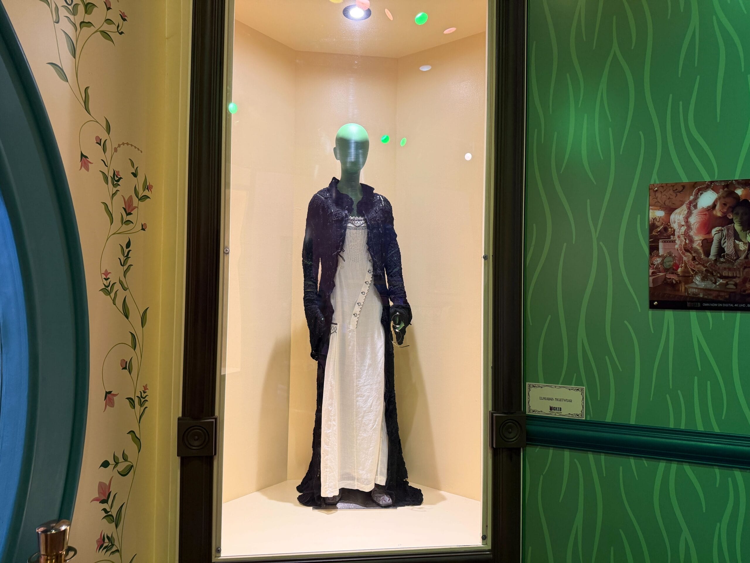 A mannequin in a glass case shows Wicked costumes, with a dramatic black and white dress, much like a Disney exhibit’s display.
