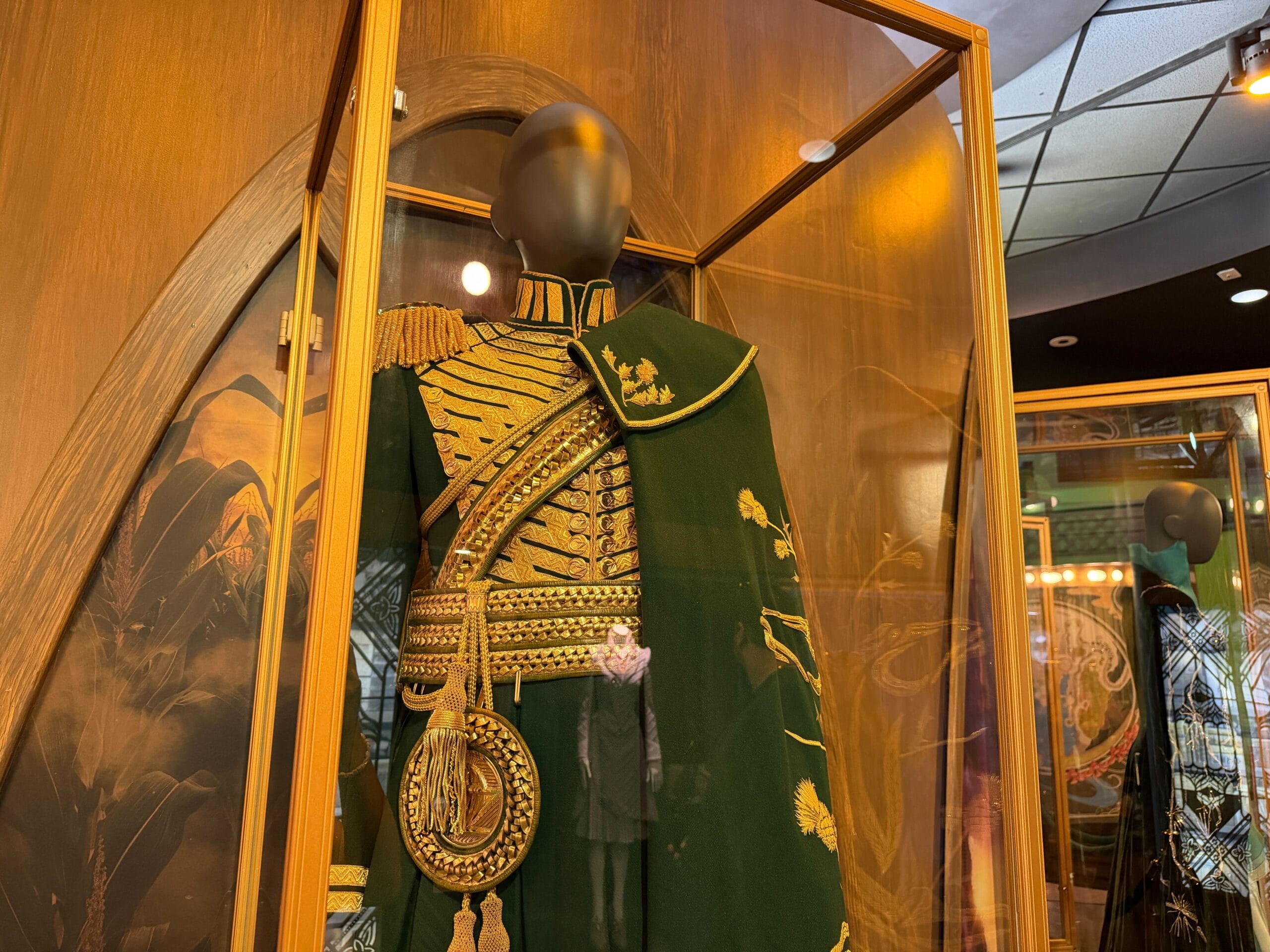 A green and gold military-style Wicked uniform on a headless mannequin inside a glass case at Universal Studios Florida, not Disney.