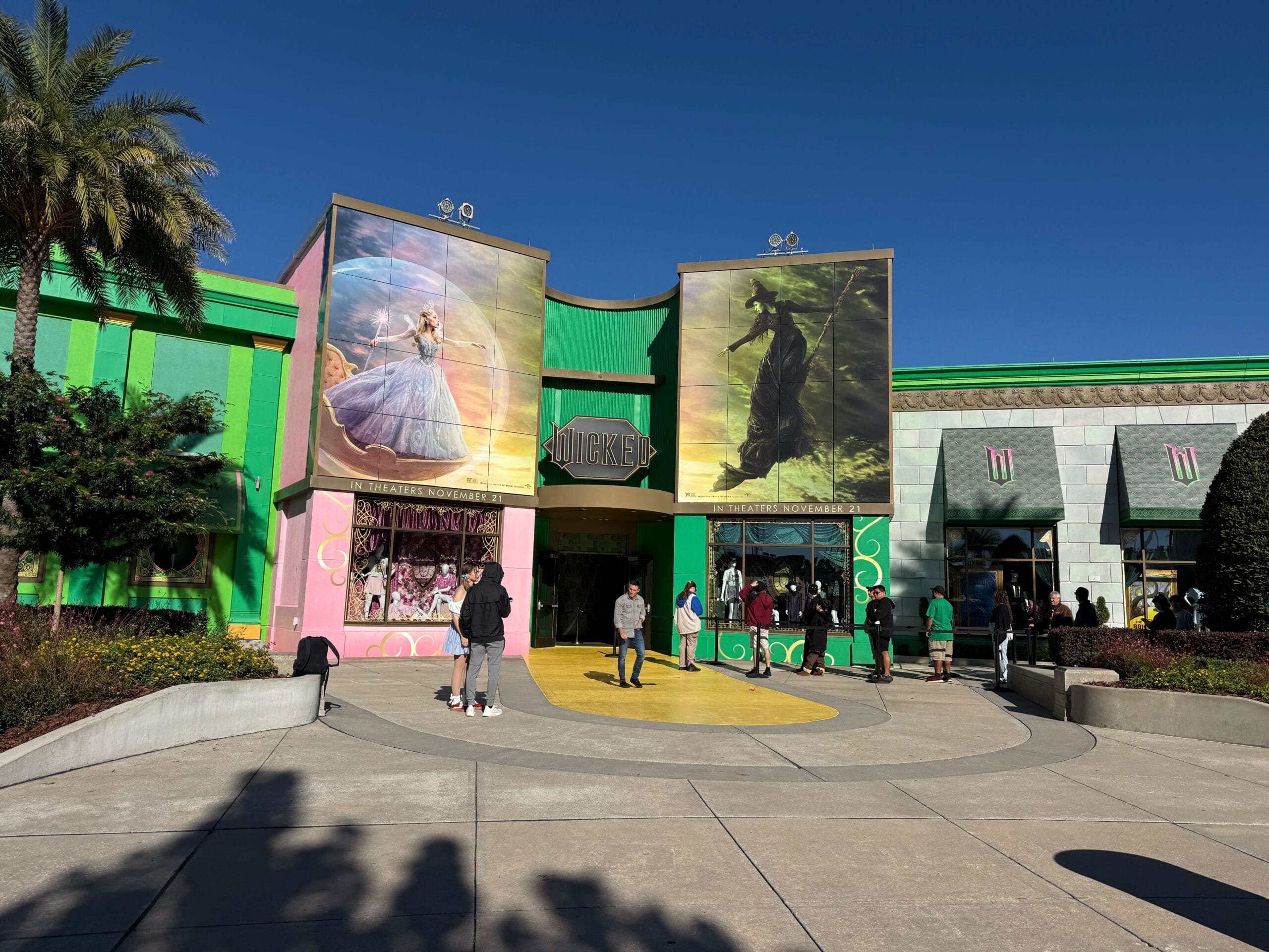 Guests gather outside a pastel green and pink building with Cinderella and Maleficent murals, evoking Disney park magic.