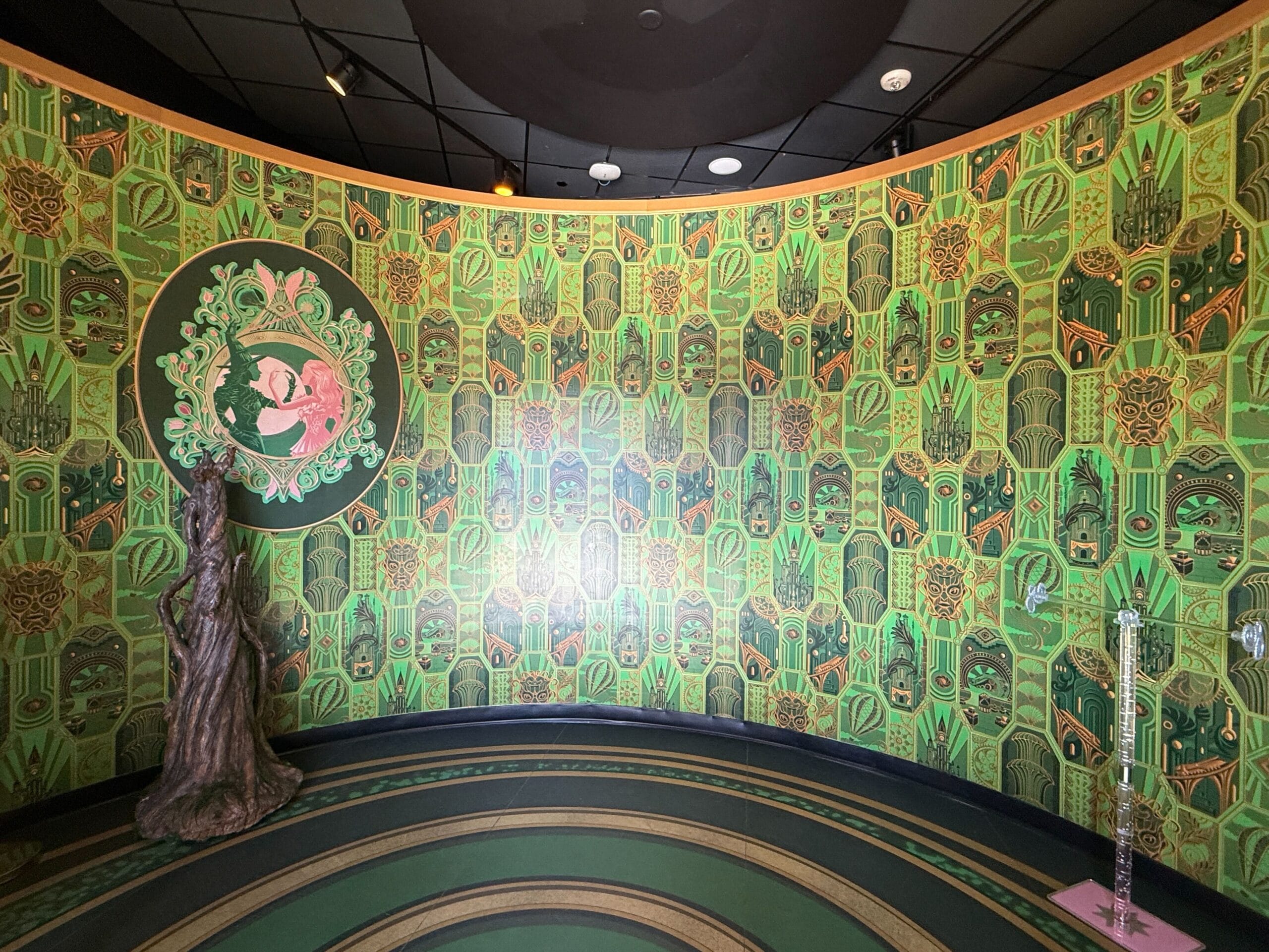 Art Deco green wallpaper with repeating patterns, a round artwork, and a statue in a curved room reminiscent of Disney park elegance.