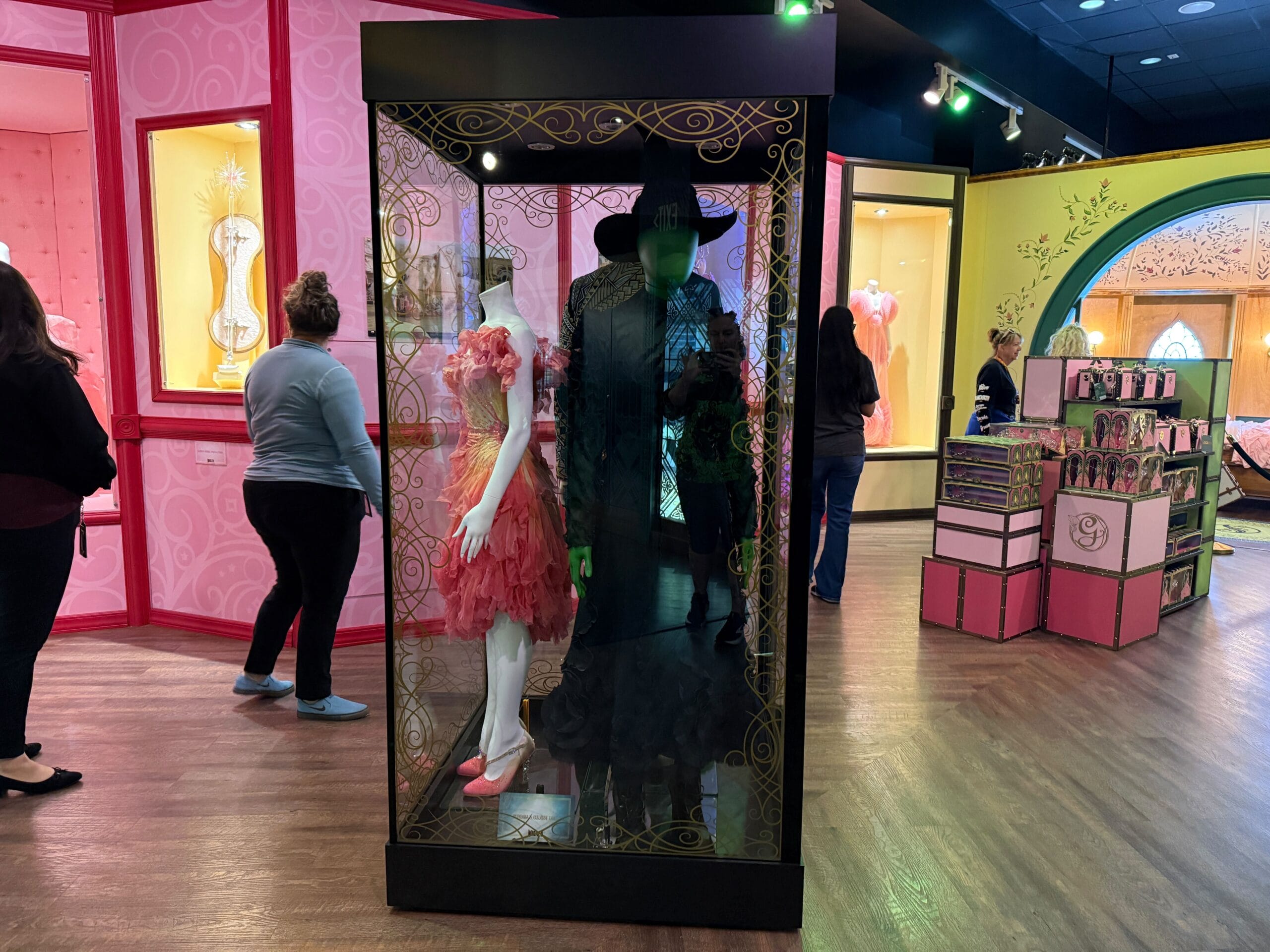 Mannequins as Glinda and Elphaba from Wicked on display, with guests exploring, like a Disney Parks exhibit minus the castle.