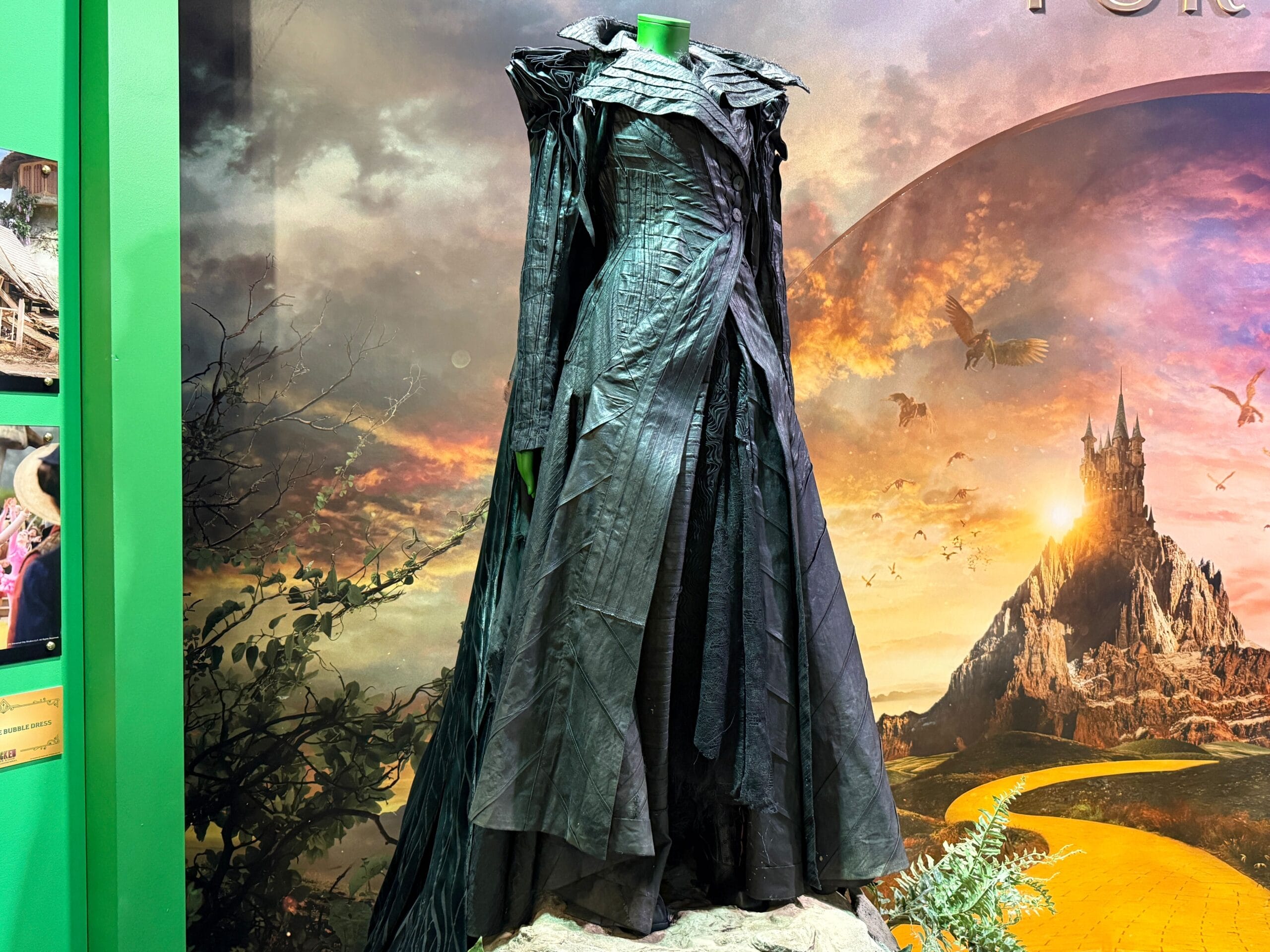 Black, dramatic, floor-length witch costume with layered shoulders, set before a castle reminiscent of Disneyland’s Sleeping Beauty Castle.