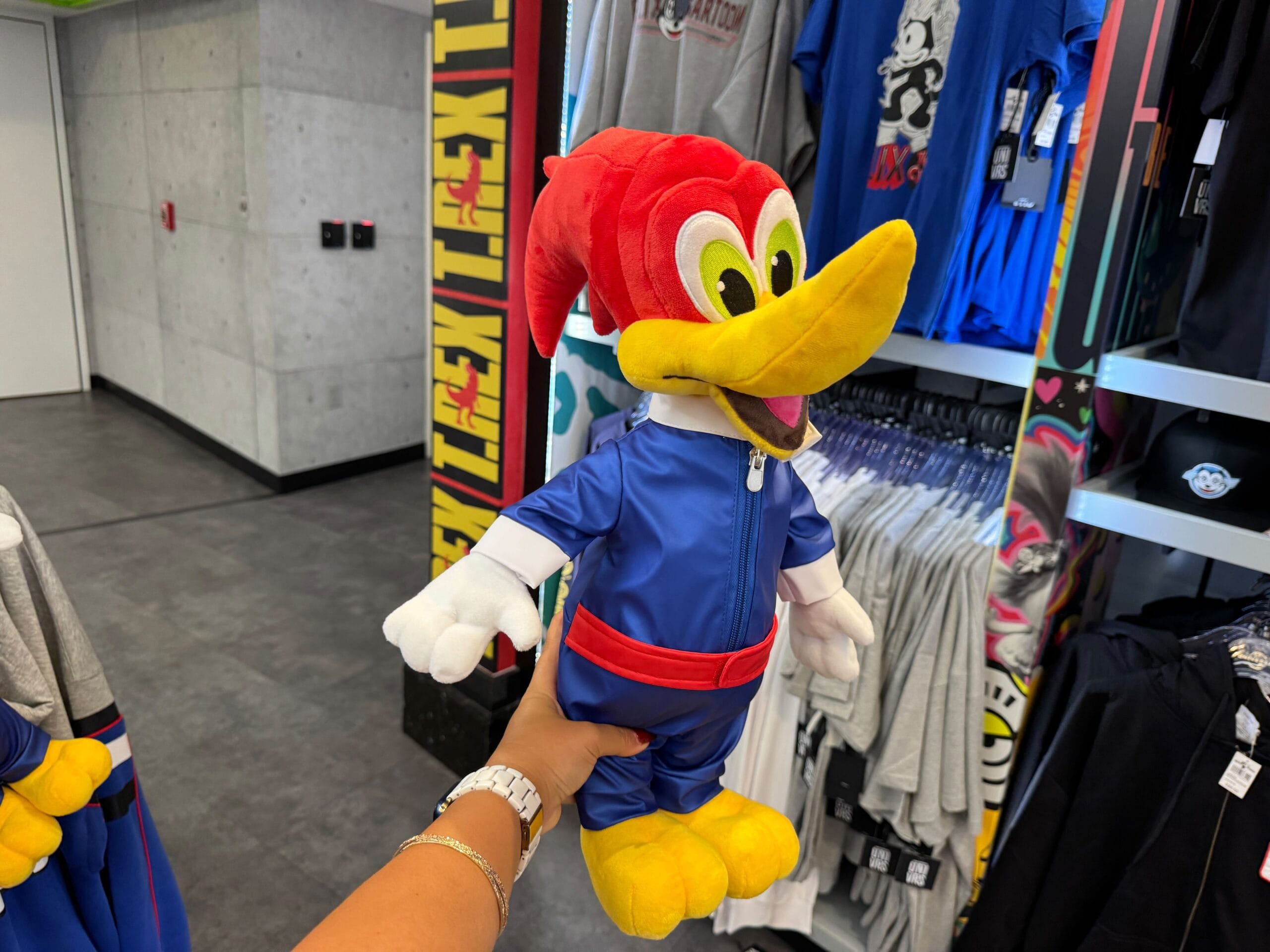 A person holds a Woody Woodpecker plush toy dressed in blue, inside a clothing store.