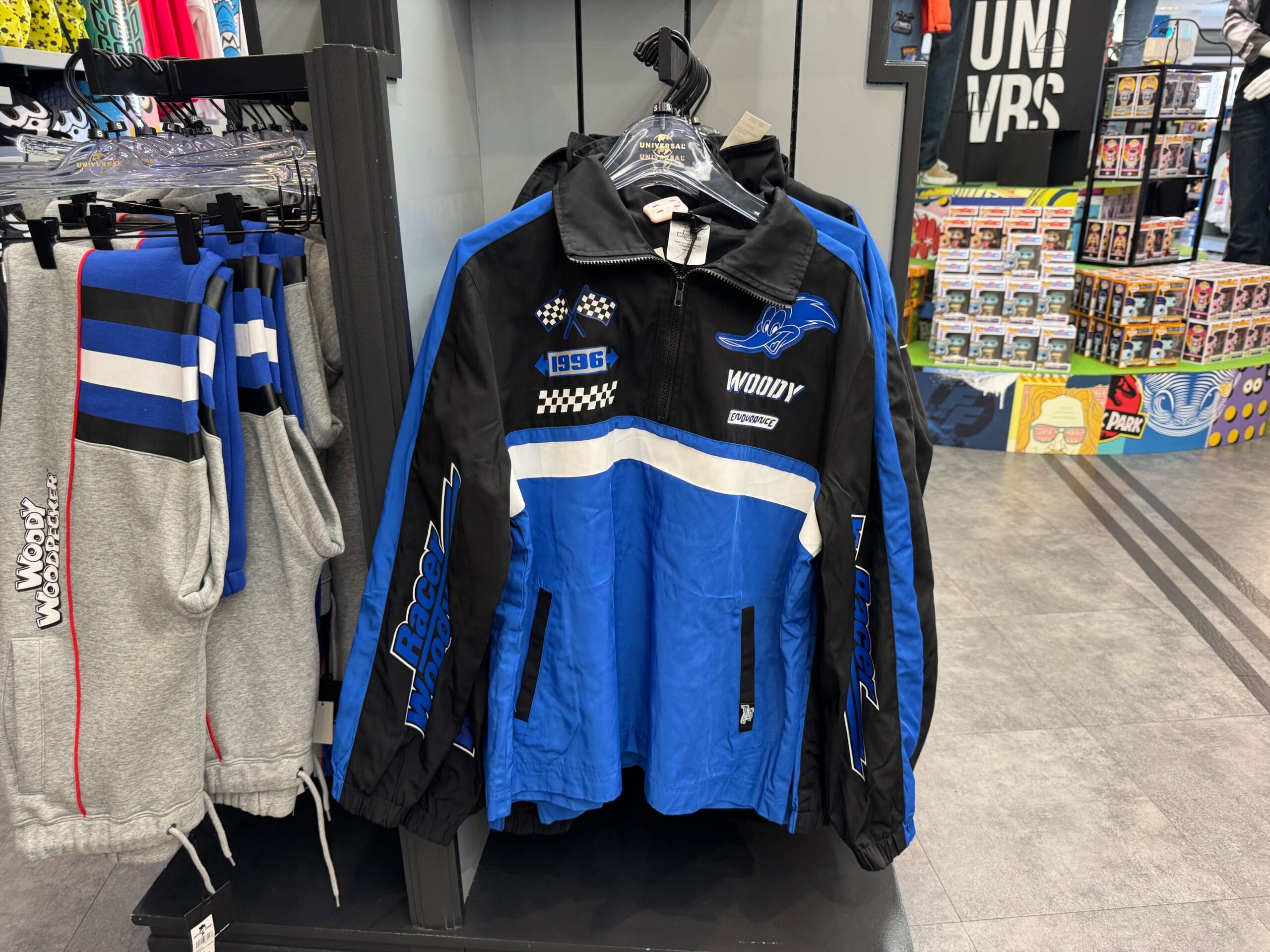 Blue and black "Woody" racing-style jacket with patches hangs on a rack in a clothing store.