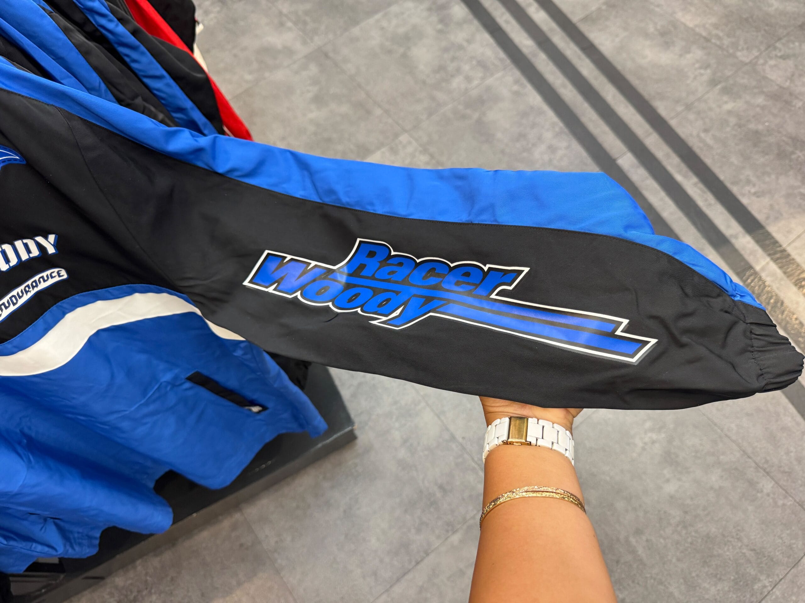 A person holds a blue and black jacket sleeve with "Racer Woody" written on it in blue and white letters.