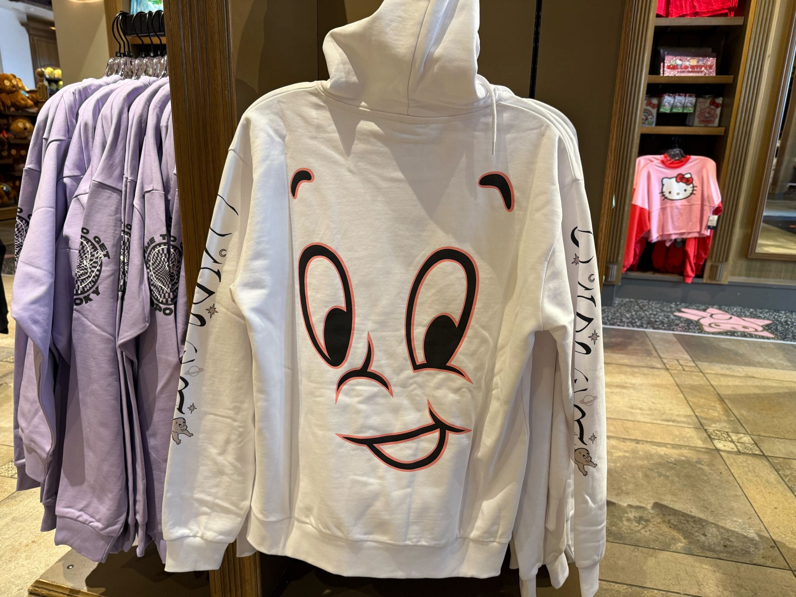 A white Casper Apparel hoodie featuring a smiling cartoon face on the back, displayed in a shop like those near Disney castle entrances.