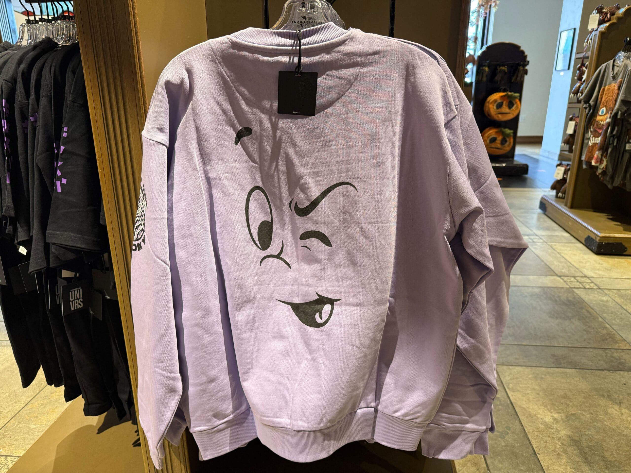 A lavender Casper Apparel sweatshirt with a winking cartoon face, displayed in a theme park store—unlike any Disney castle merch.