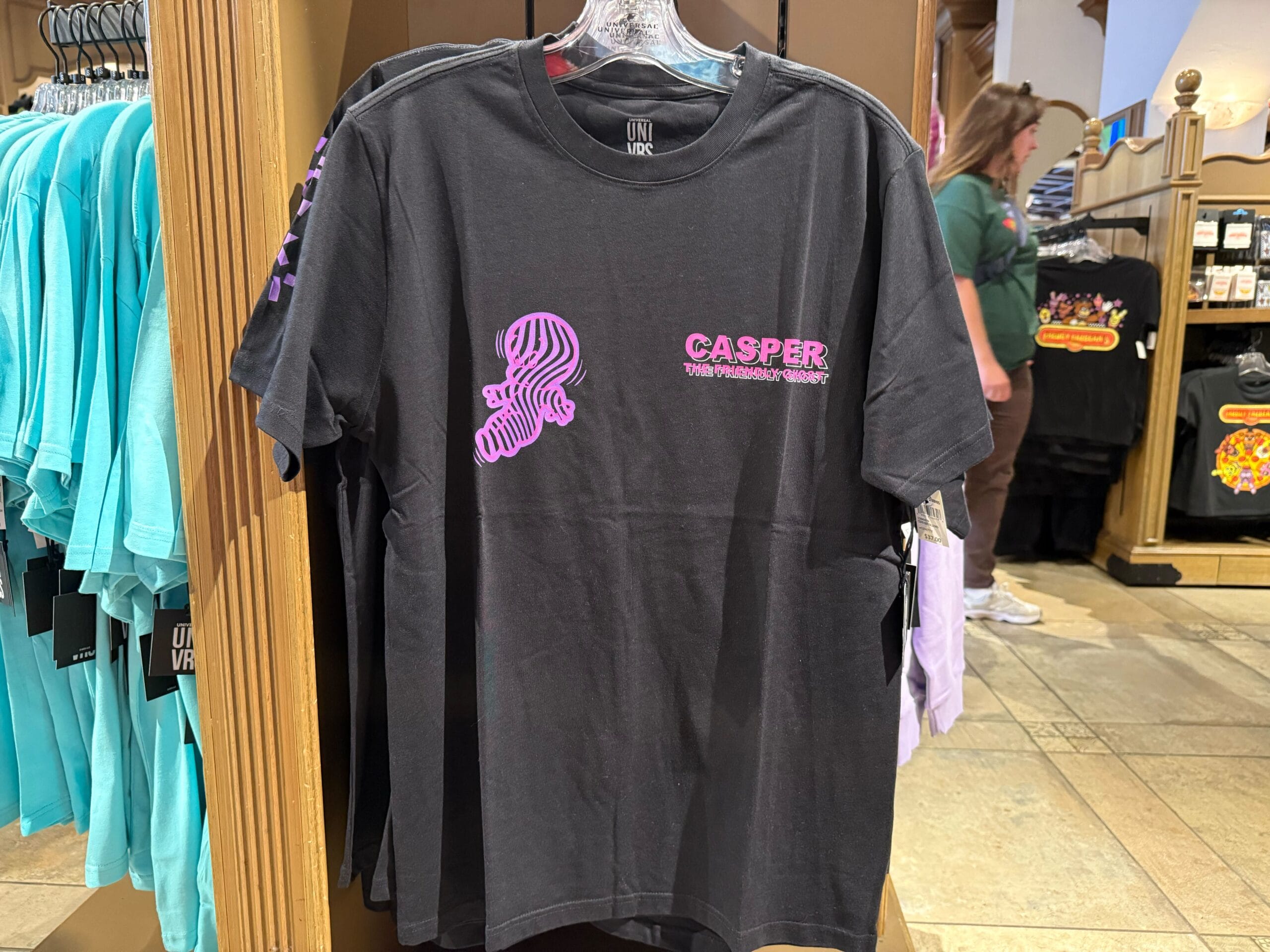 Black "Casper the Friendly Ghost" tee with pink logo, from Casper Apparel, displayed at Universal Studios—not a Disney Park castle.