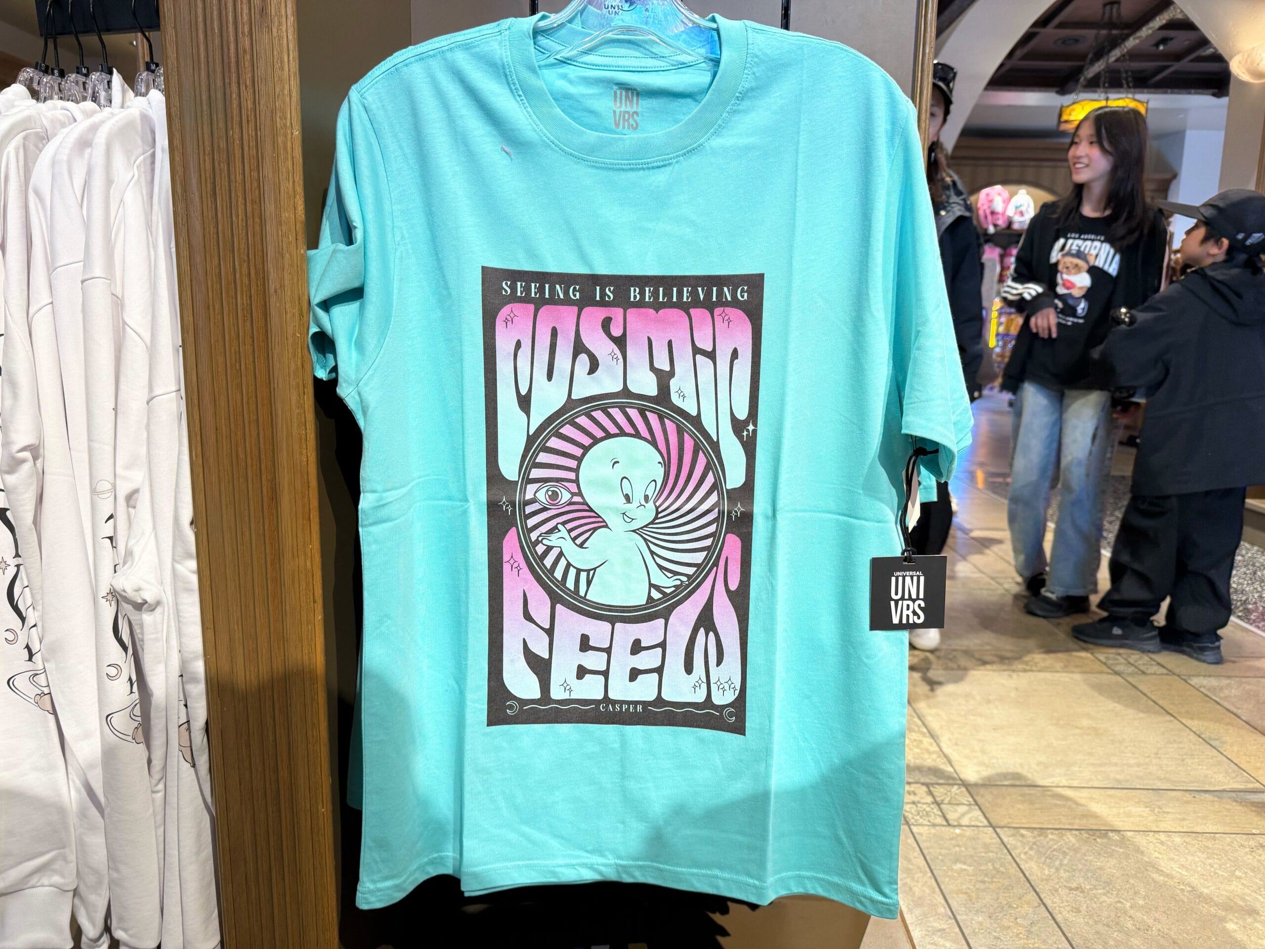 A turquoise Casper Apparel tee with a retro "Cosmic Feels" alien design—not unlike the playful style at Tomorrowland in Disney Parks.