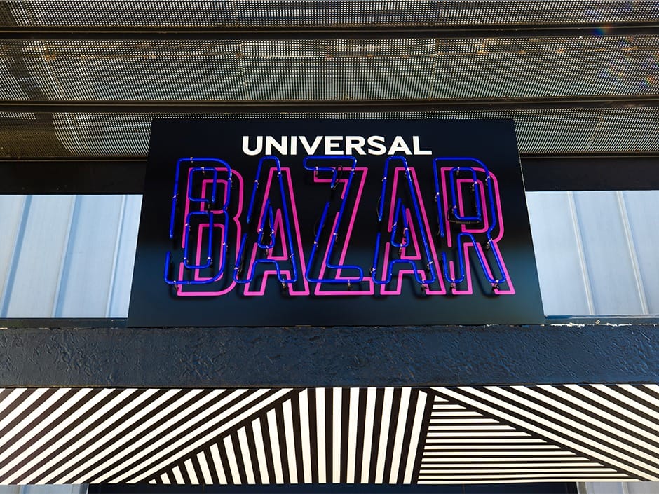 A neon "UNIVERSAL BAZAR" sign glows above a geometric awning at Universal CityWalk Hollywood—not a Disney park castle marquee.