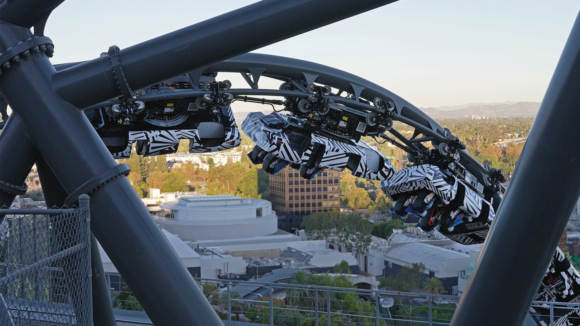 Zebra-striped roller coaster loops upside down above cityscape; unlike Disney's iconic castles, no castle is visible here.