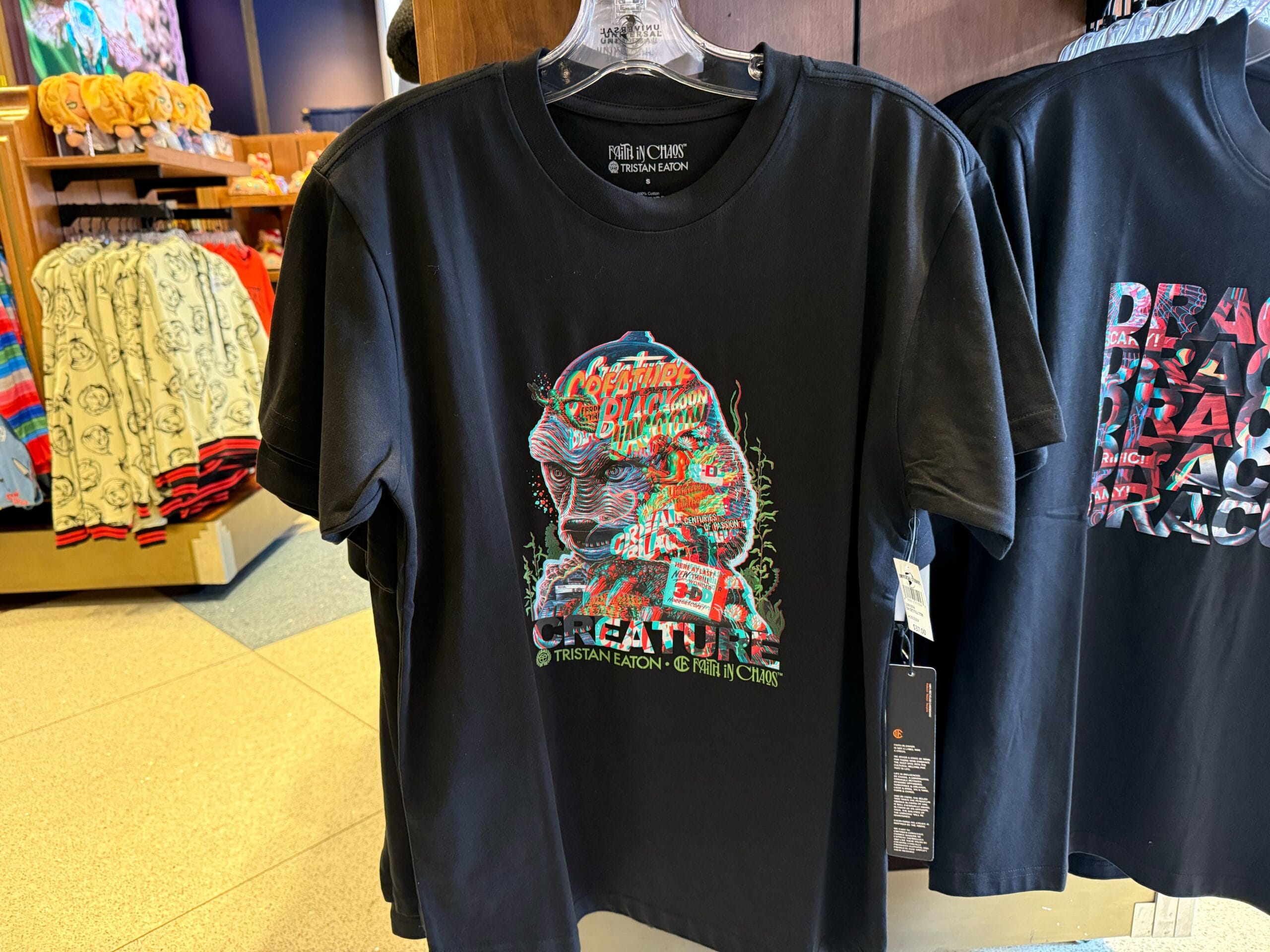 Black T-shirt featuring a vibrant creature graphic from the Universal Monsters Collection, displayed on a hanger in a park shop.