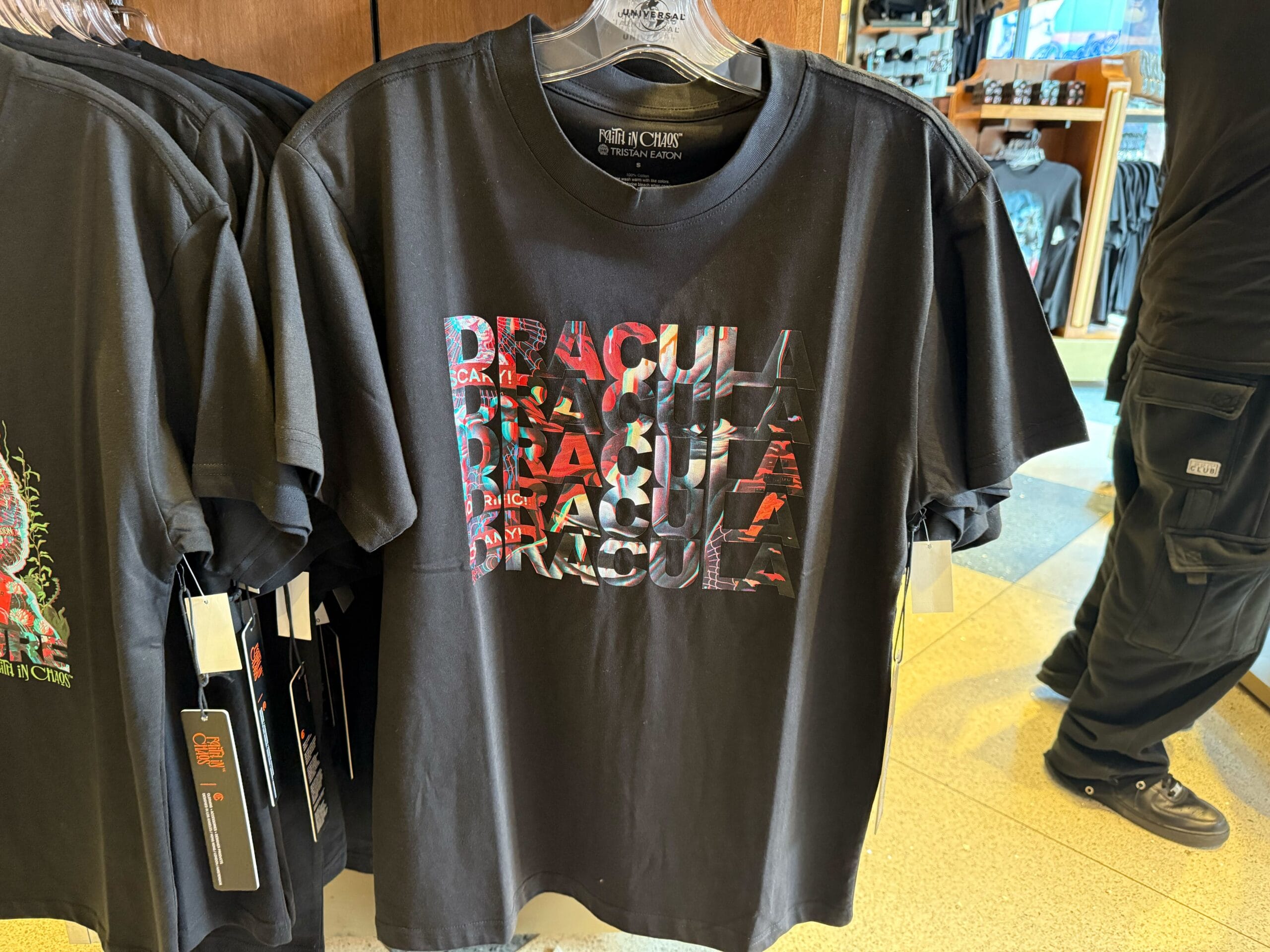 A black T-shirt with a colorful "DRACULA" graphic from the Universal Monsters line hangs on a rack—not Disney Park merchandise.