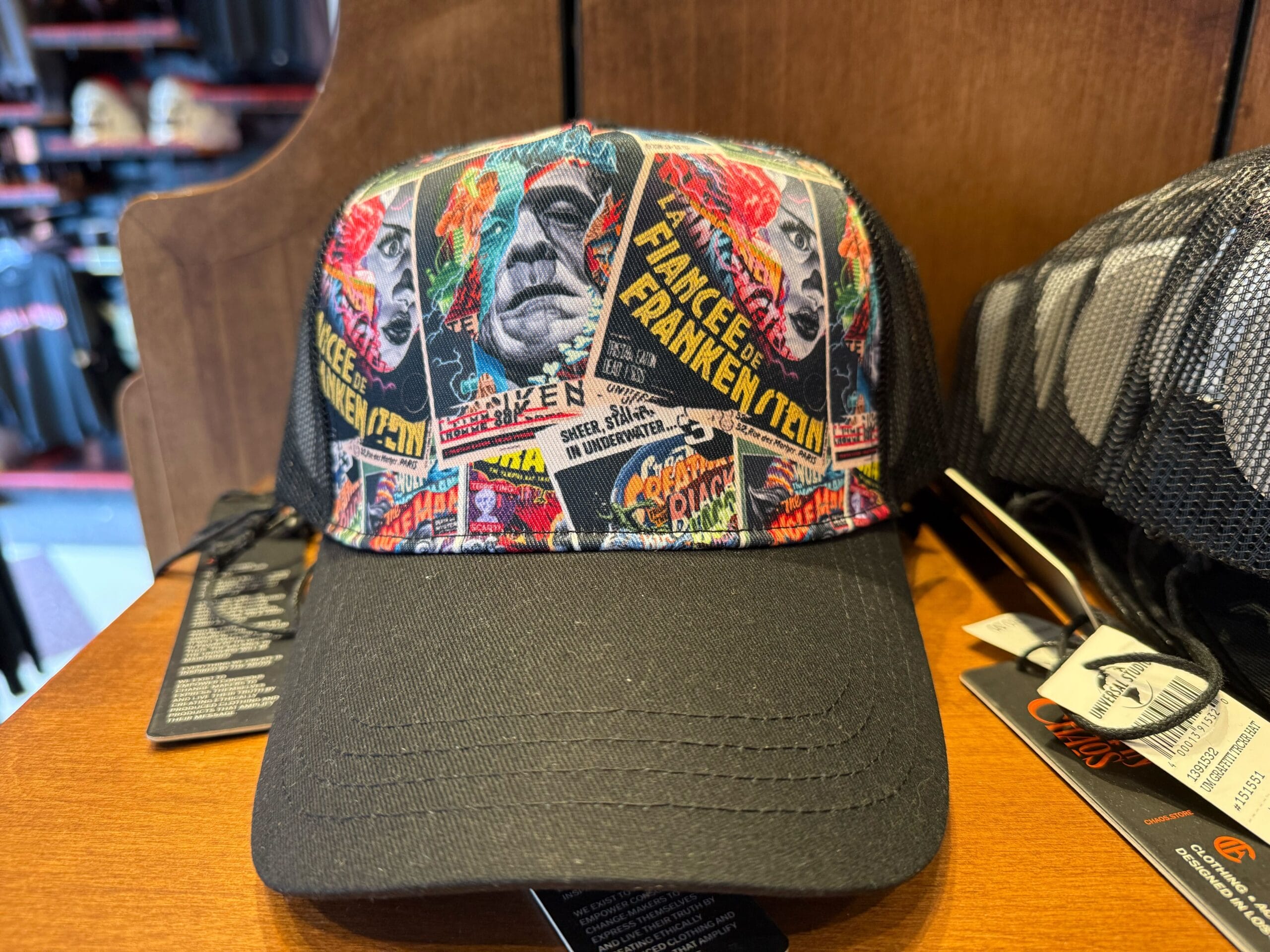 A trucker hat with vibrant vintage Frankenstein designs, reminiscent of retro park merch, displayed on a wooden shelf.