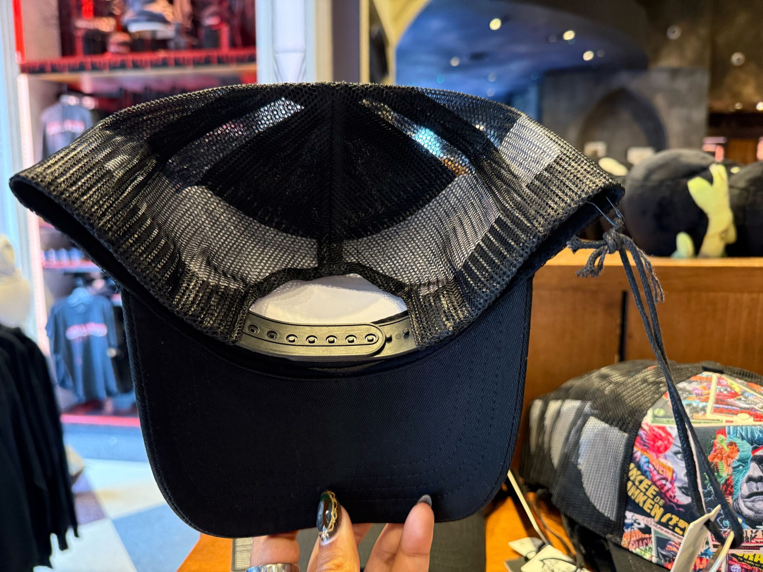 A person holds a black mesh-back Universal Monsters cap inside a store with clothing, not featuring Disney Park icons or castles.