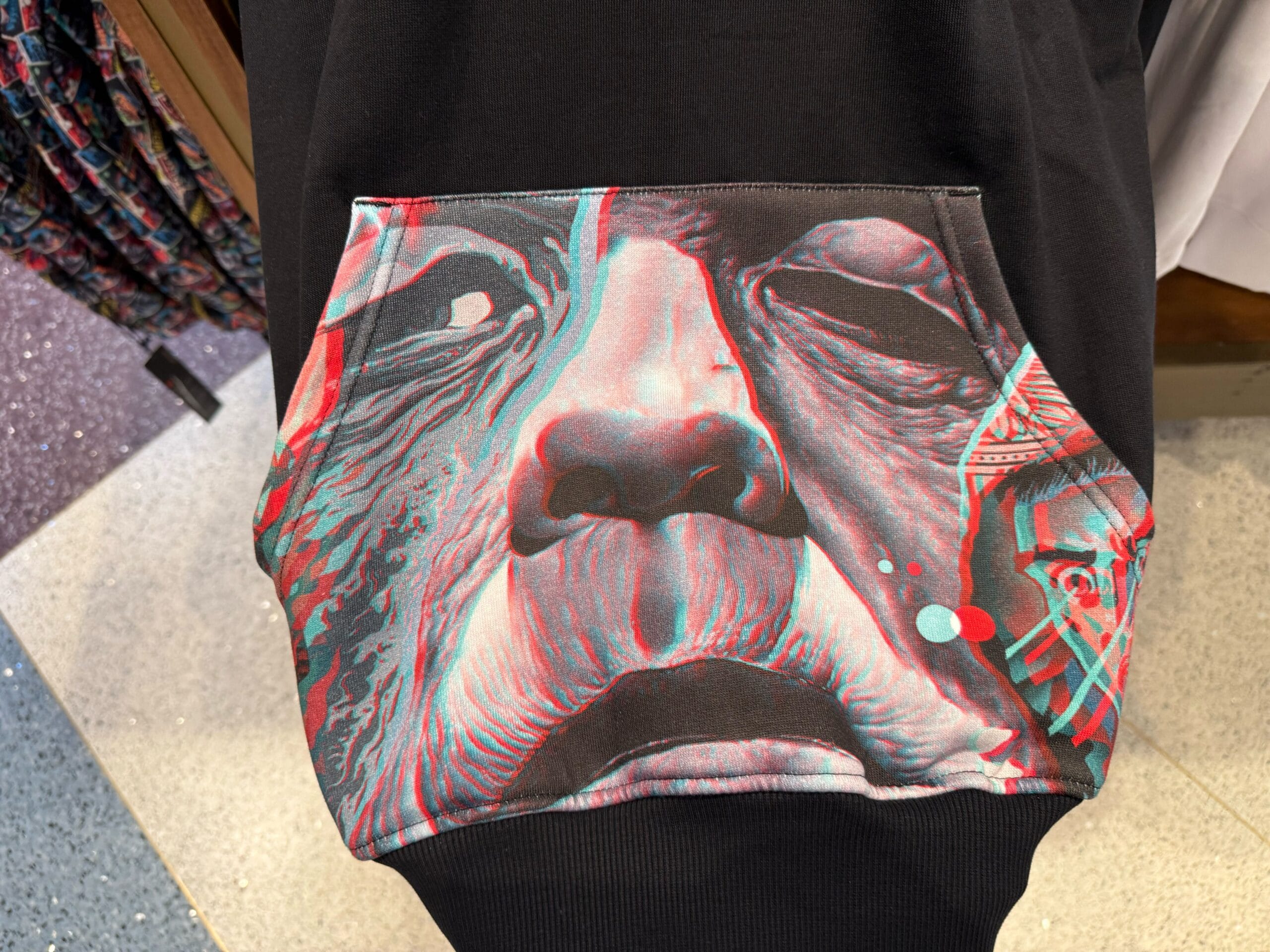 A detailed shot of a hoodie pocket from the Universal Monsters Collection shows a vibrant, abstract face with bold, 3D-style effects.