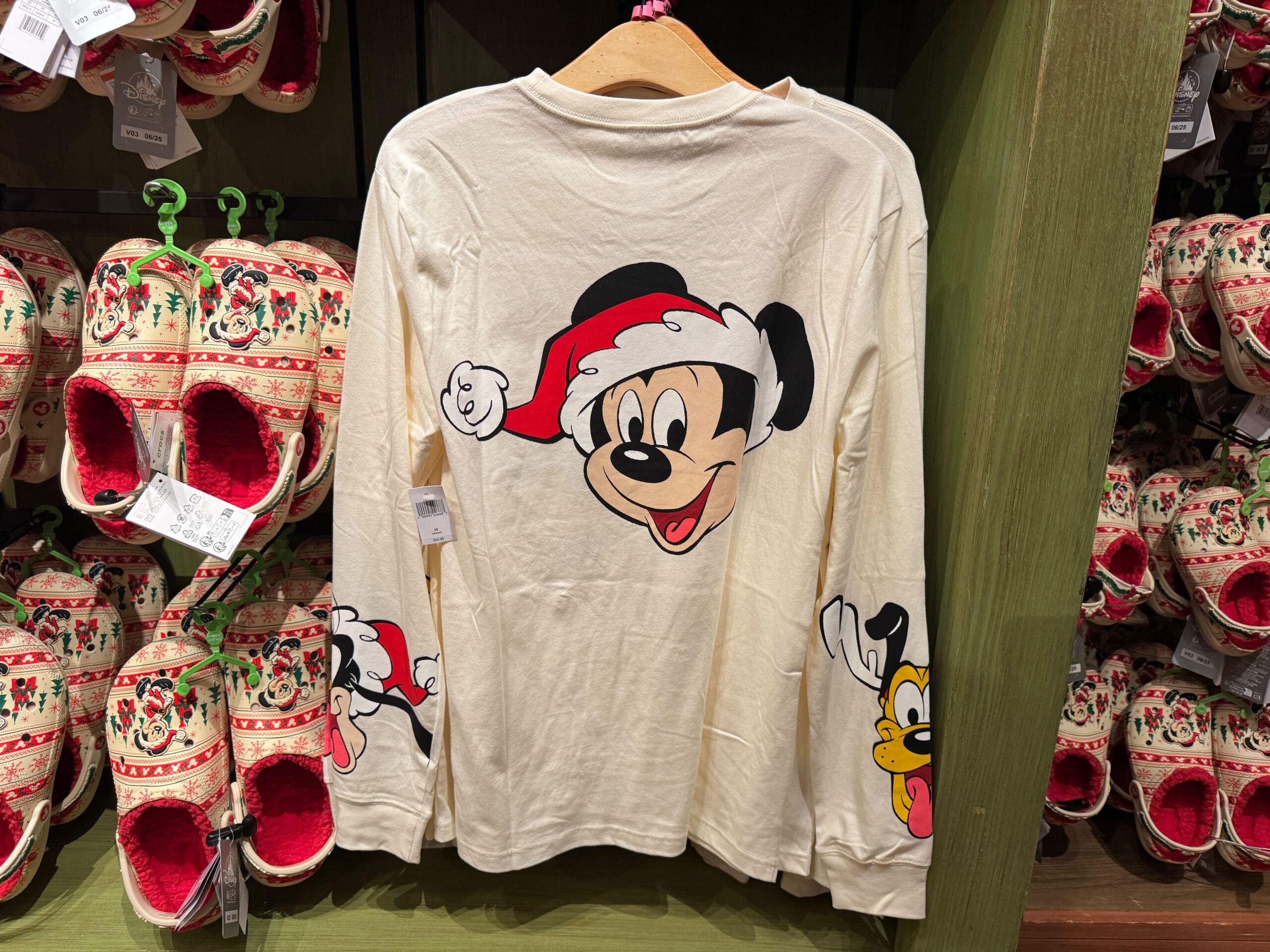 Long-sleeve holiday shirt with Mickey Mouse in a Santa hat, part of the 2025 Christmas merchandise display.