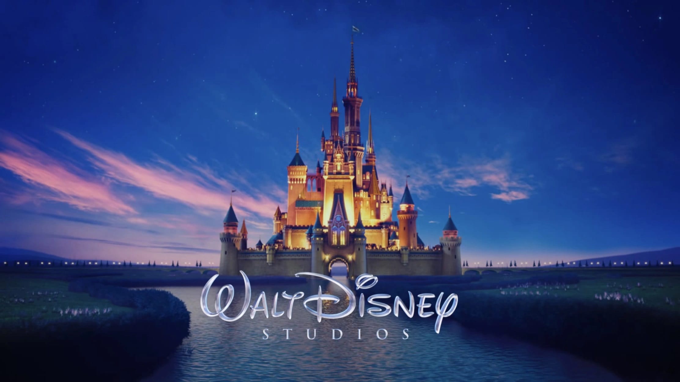 Illuminated Disney castle at night with "Walt Disney Studios" over a river, perfect for fans of Disney and Impossible Creatures.
