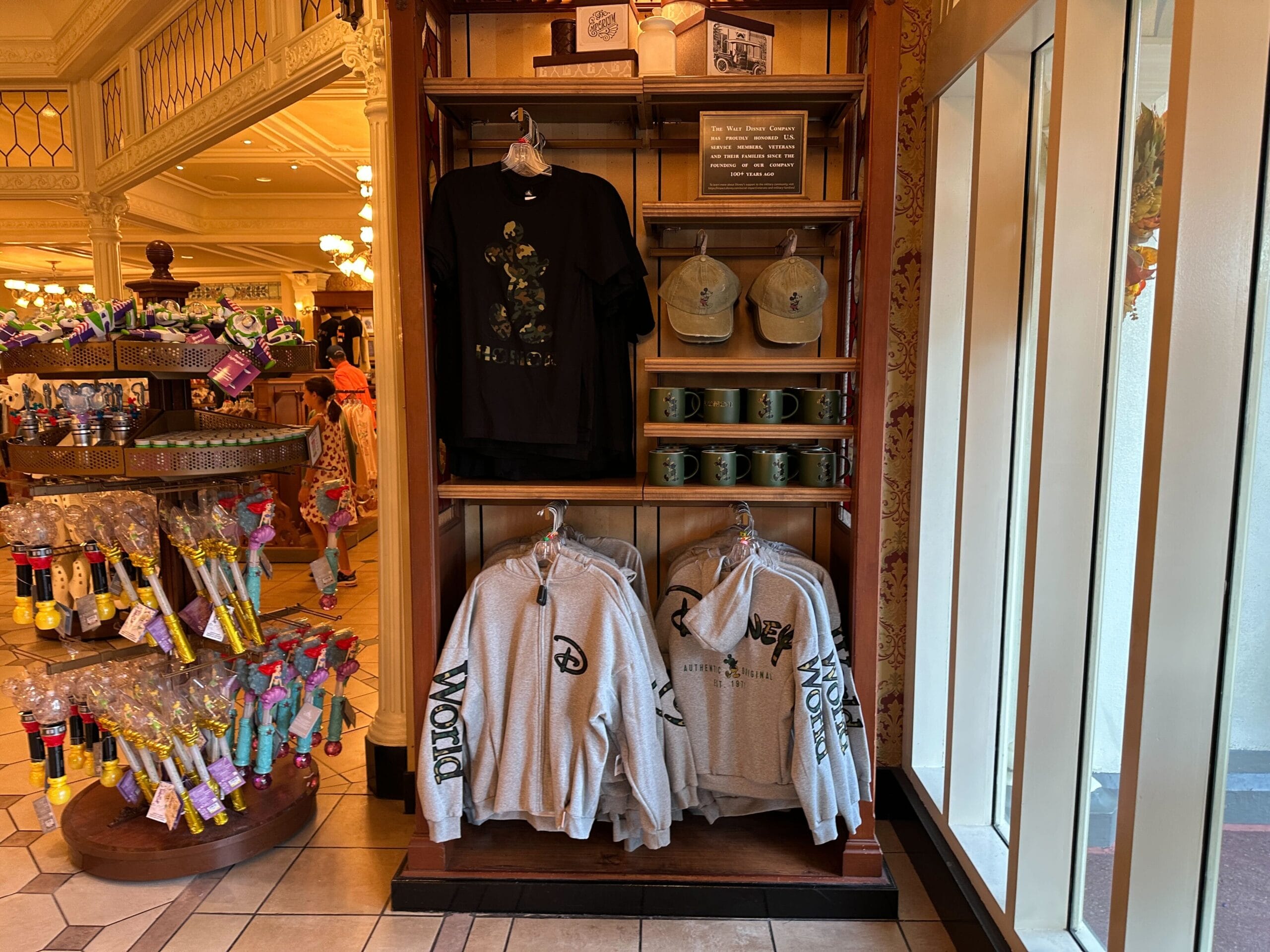 Disney Parks shirts, hats, and mugs on wooden shelves in a shop near a window, reminiscent of Main Street USA boutiques.