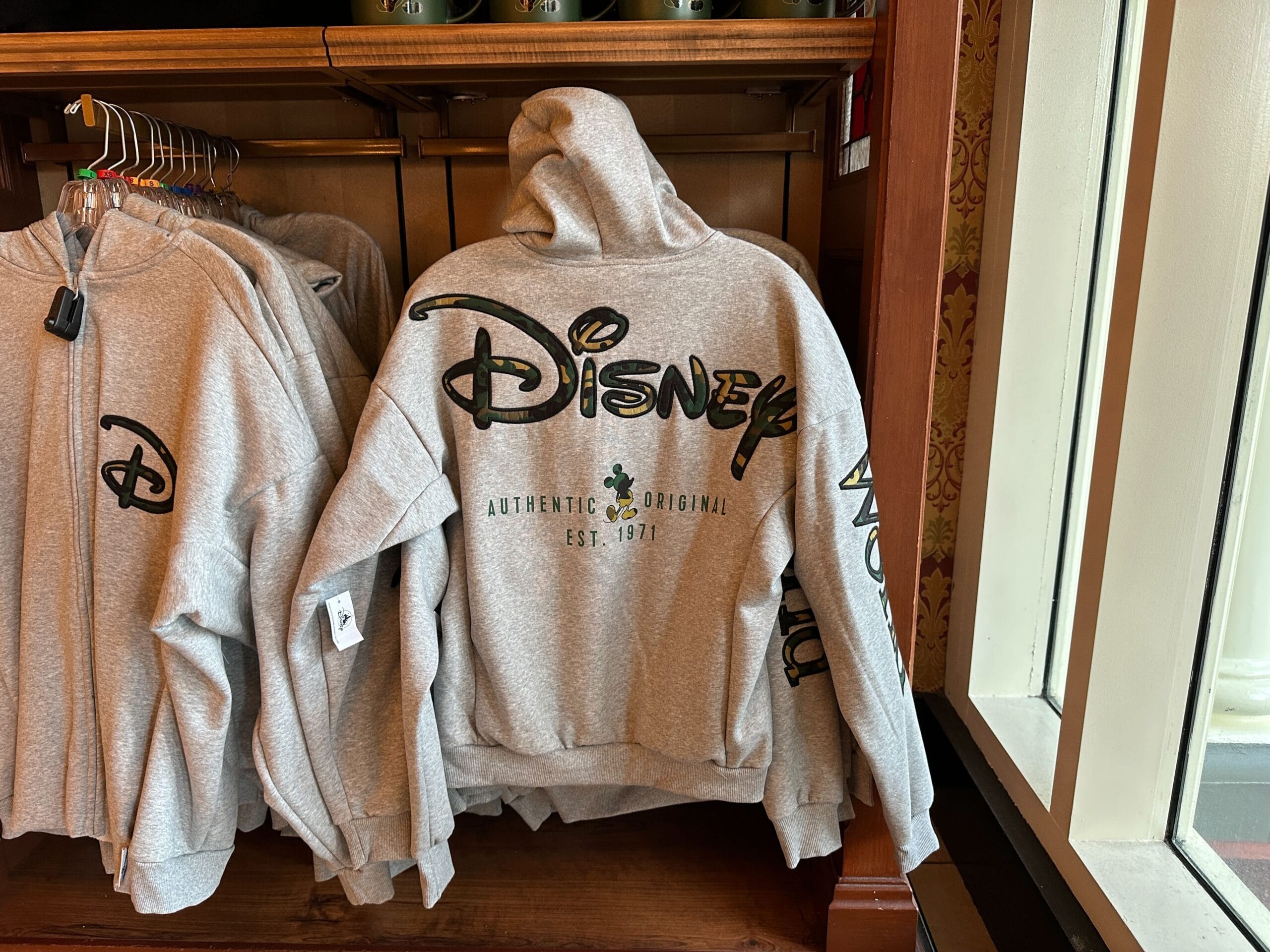 Gray Disney hoodie featuring Mickey Mouse and "Authentic Original Est. 1928" text, spotted on a rack at a Disney park store.