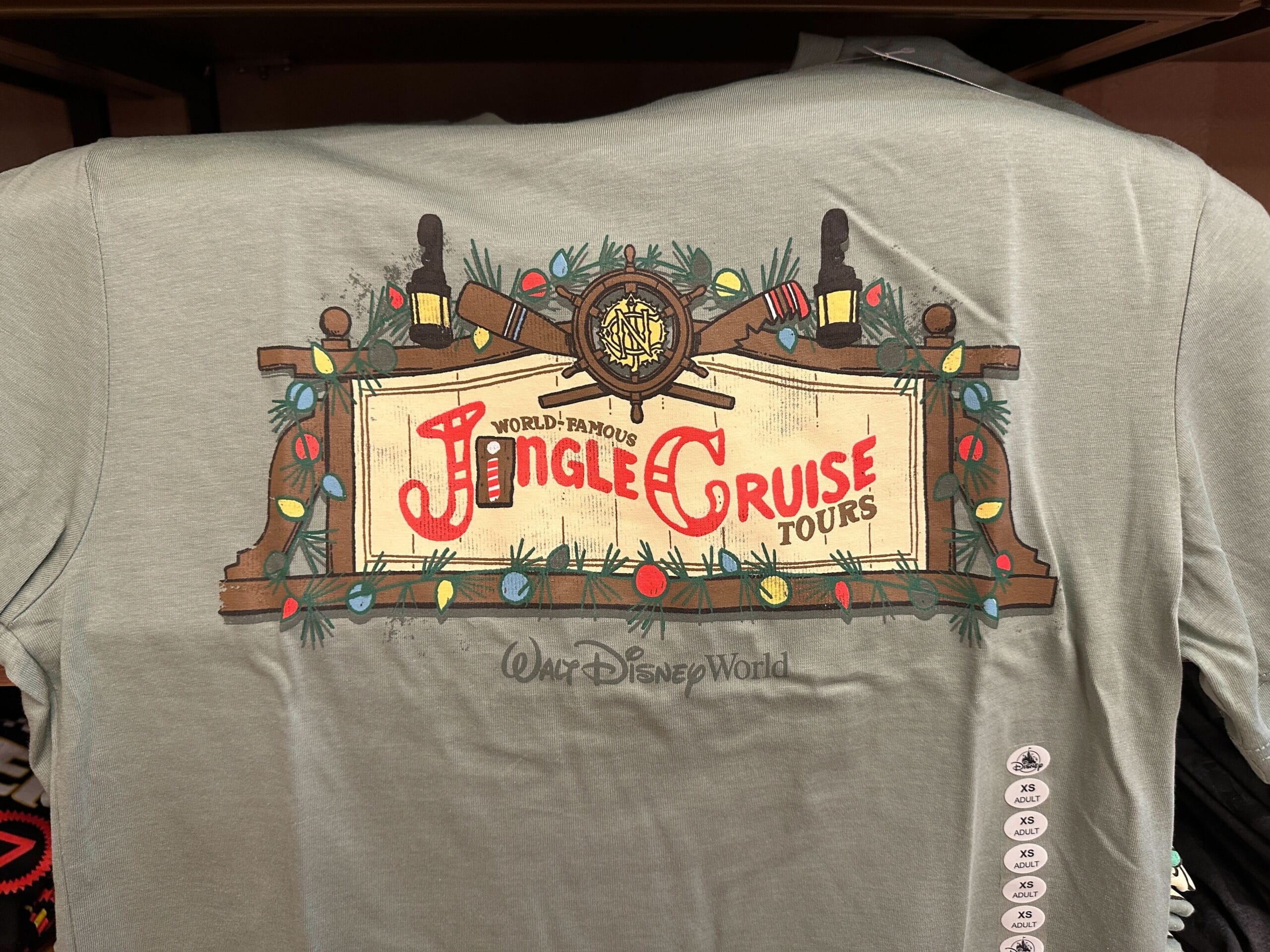 Green shirt at Walt Disney World featuring a festive "Jingle Cruise Tours" sign, accented by colorful holiday lights.