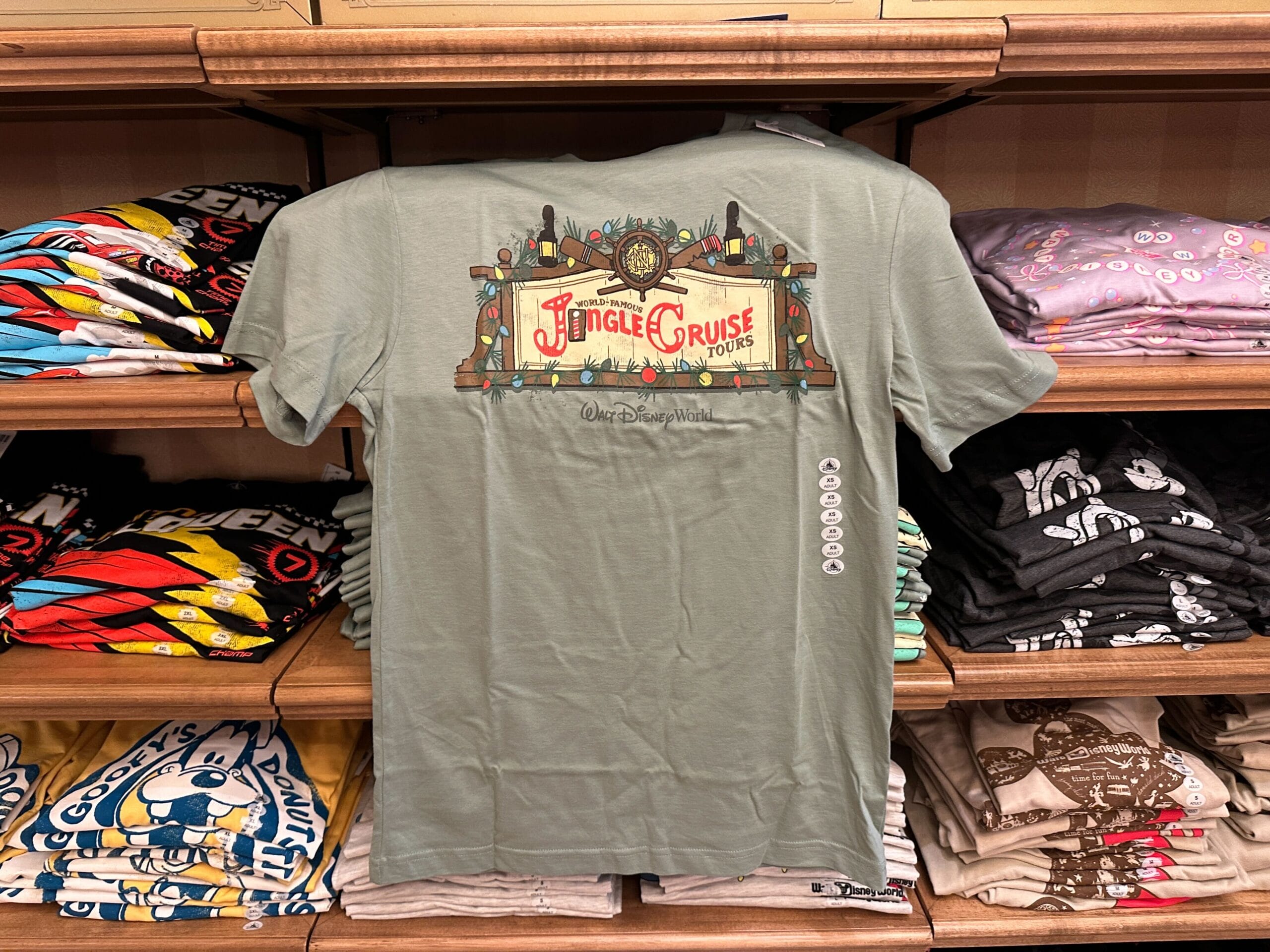 Green Jungle Cruise Tours t-shirt on a shelf among folded Disney shirts, evoking classic Adventureland from Disney parks worldwide.