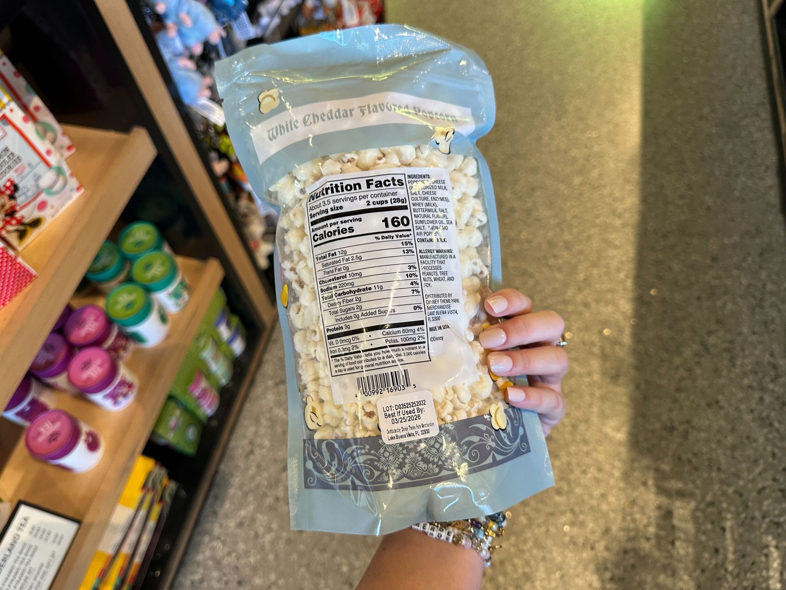 Hand holding Disney park white cheddar popcorn bag in a souvenir shop, nutrition facts visible, but no castle spotted nearby.