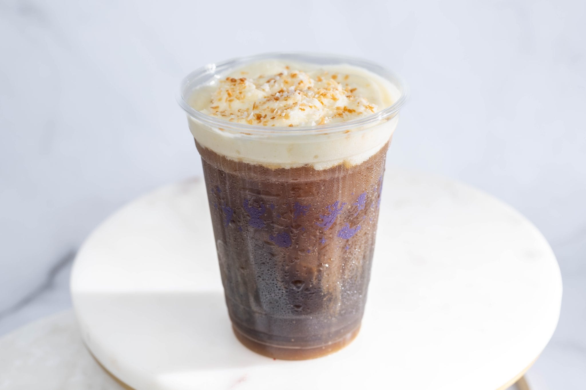 Indiana Jones Cold Brew in a clear plastic cup, topped with creamy foam and a sprinkle of crushed nuts.