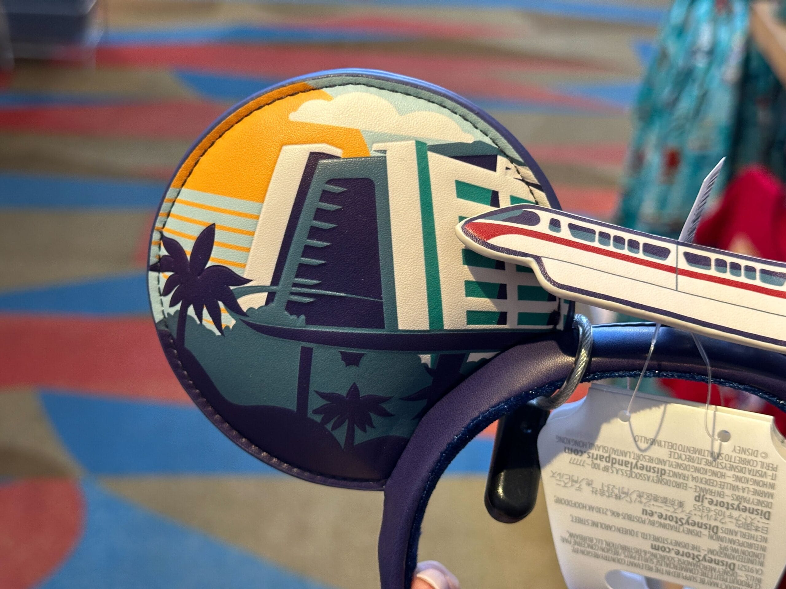 Mickey ears decorated with a sunset scene of a hotel, palm trees, and a Disney monorail, evoking classic Disneyland vibes.