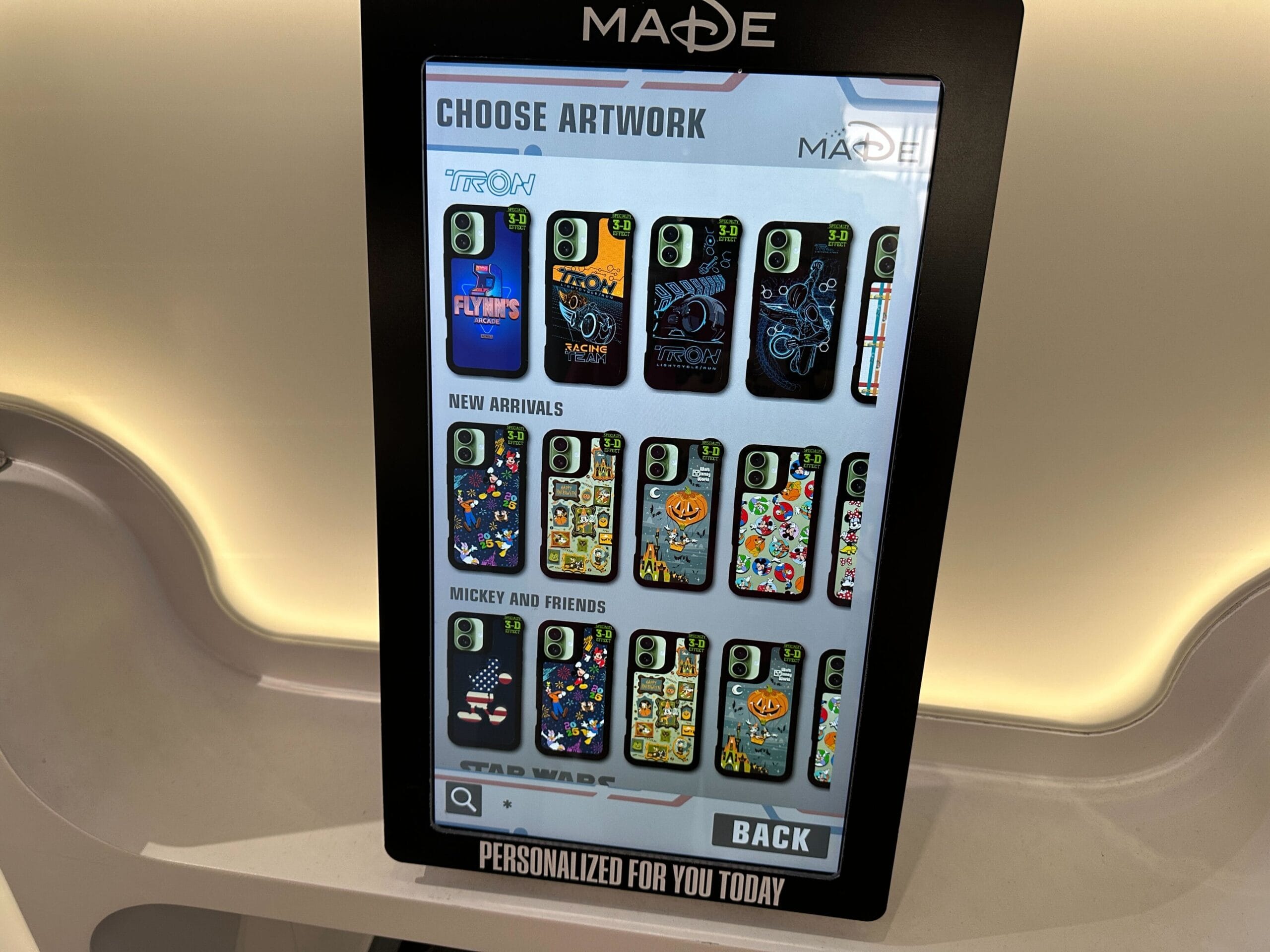 A touchscreen display at a Disney Park features customized phone cases with beloved characters and castles from worldwide Disney parks.