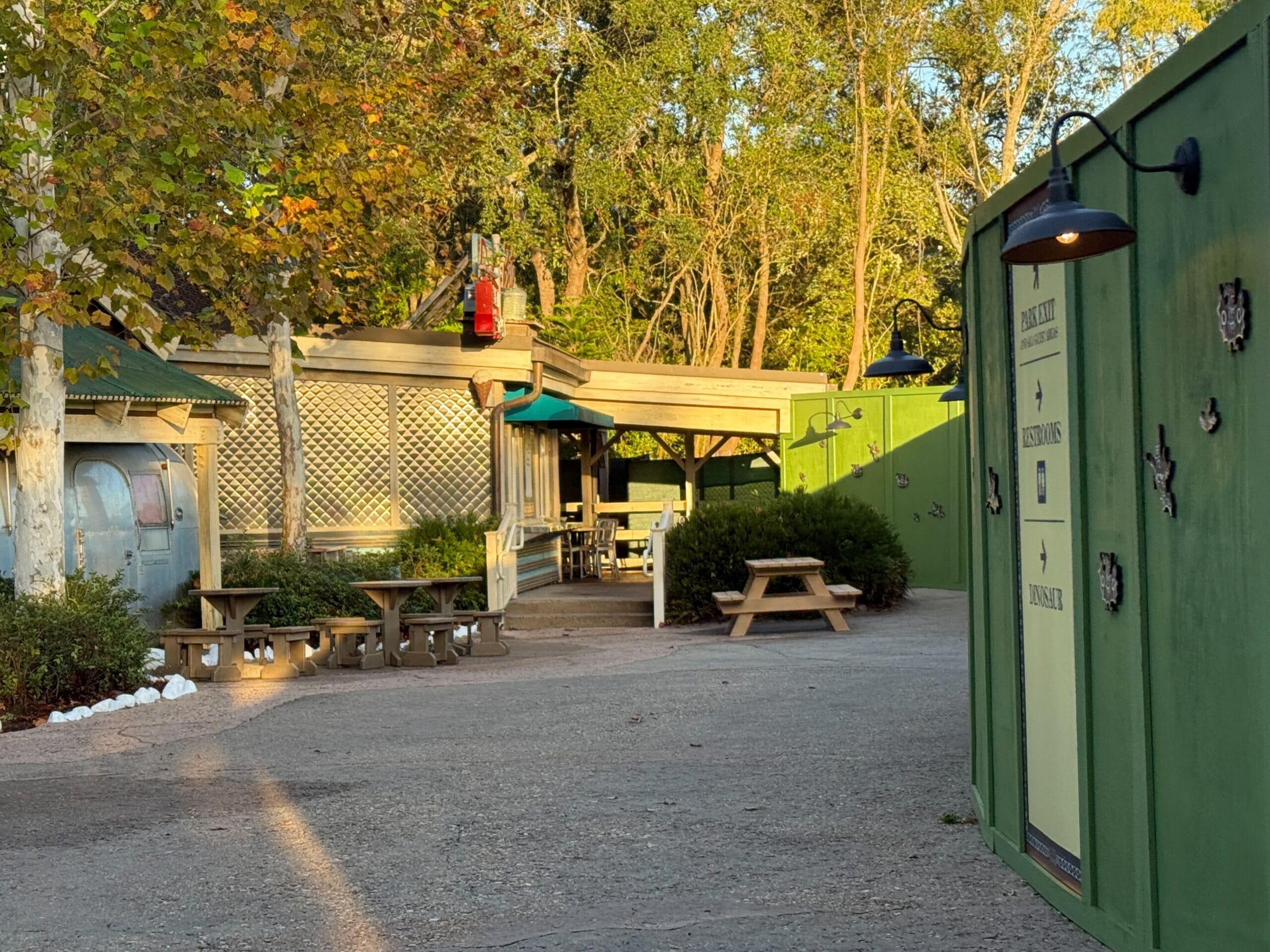 Magical outdoor dining area with picnic tables, lush greenery, and string lights, evoking Disney park charm at golden hour.