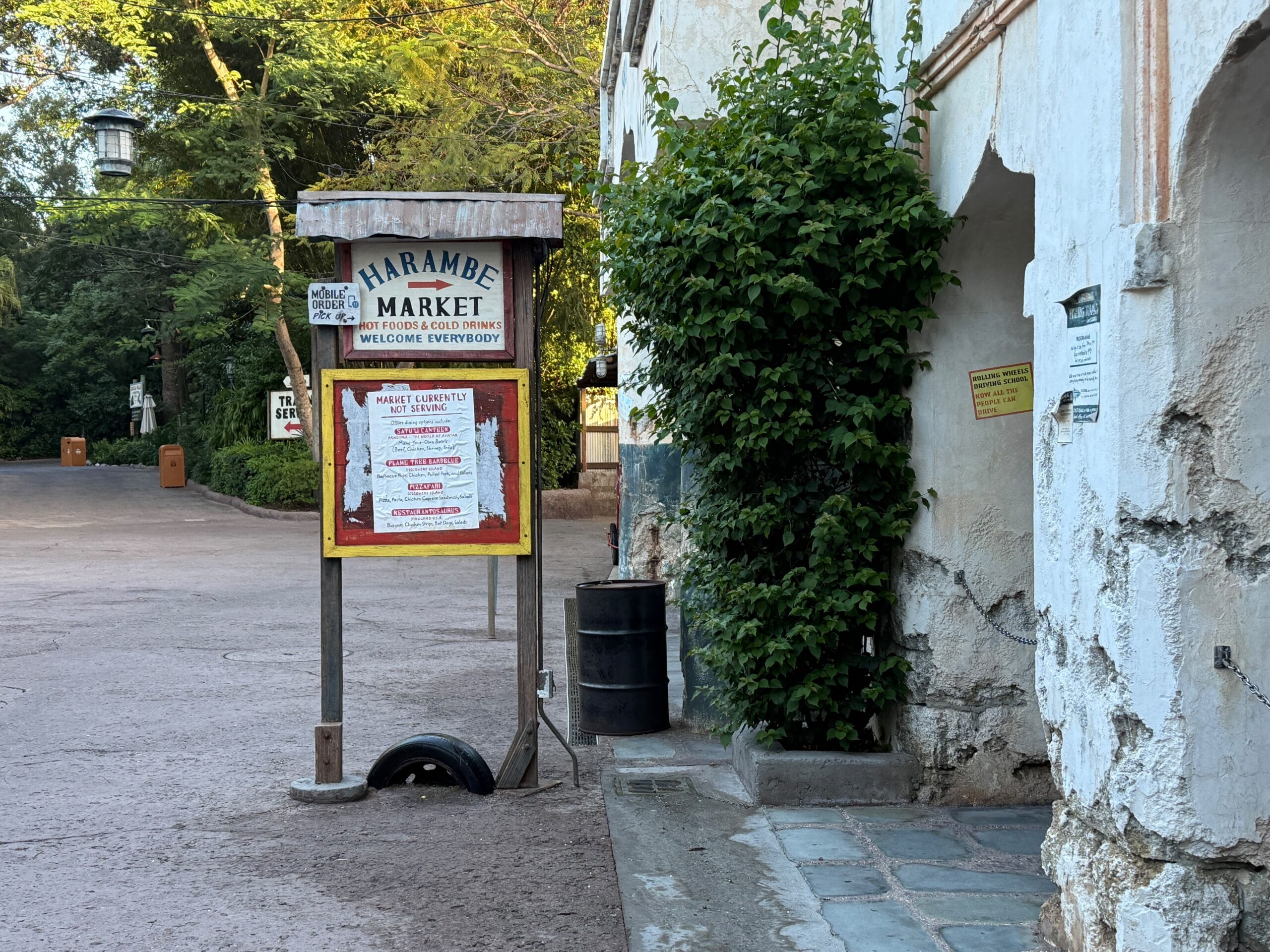 A Harambe Market sign on a peaceful path in Disney's Animal Kingdom, near an aged building and lush greenery—no castle in sight.