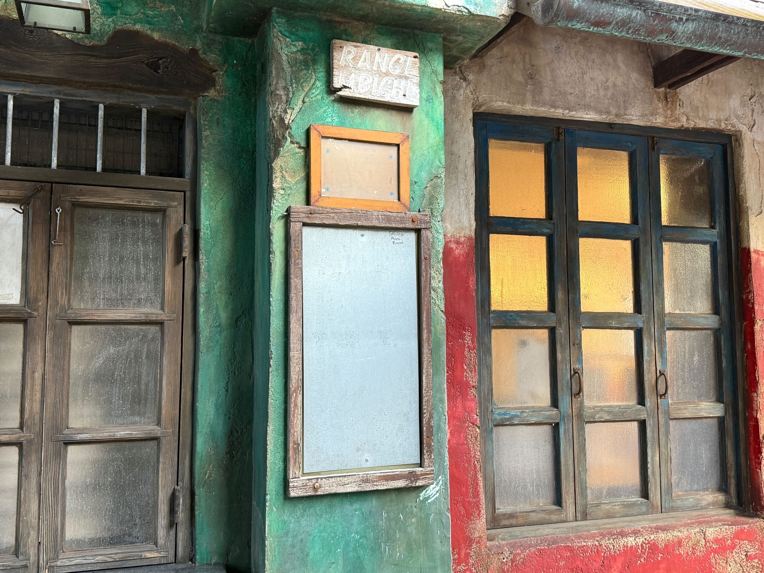 Old building with faded green and red walls, wooden door, window, and Dino-Bite Snacks-style sign in Disney's Animal Kingdom.