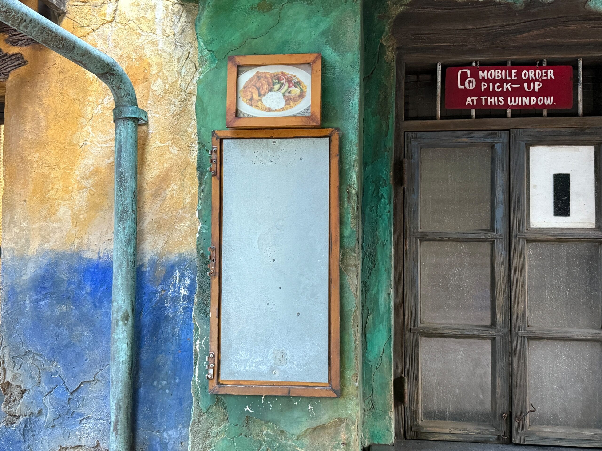 An aged wall at Dino-Bite Snacks in Animal Kingdom, with faded menu, food image, and a pick-up sign—quintessential Disney detail.