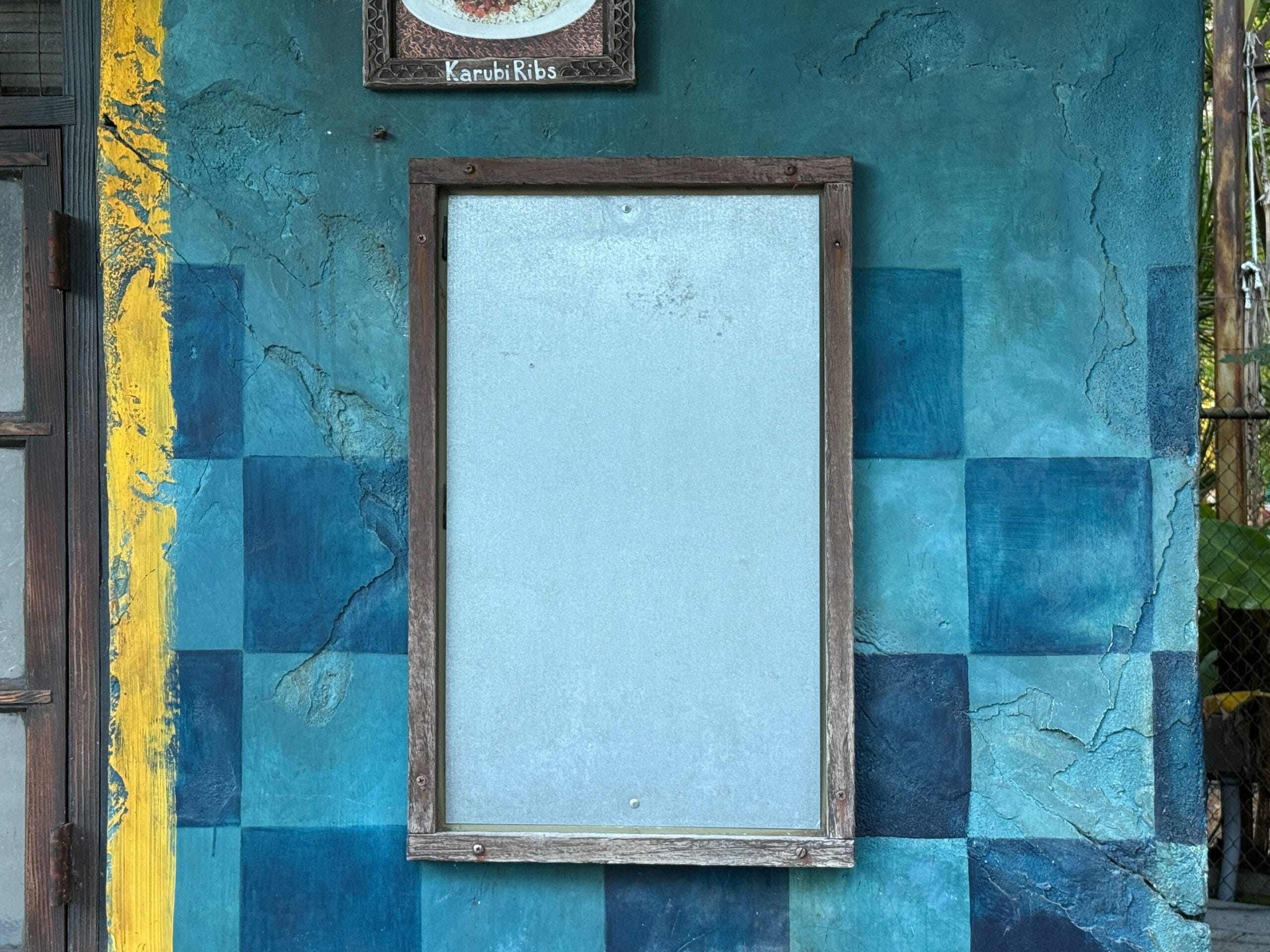 A wooden-framed empty notice board on a textured blue wall at Disney's Animal Kingdom, no castle like any Disney park’s in view.