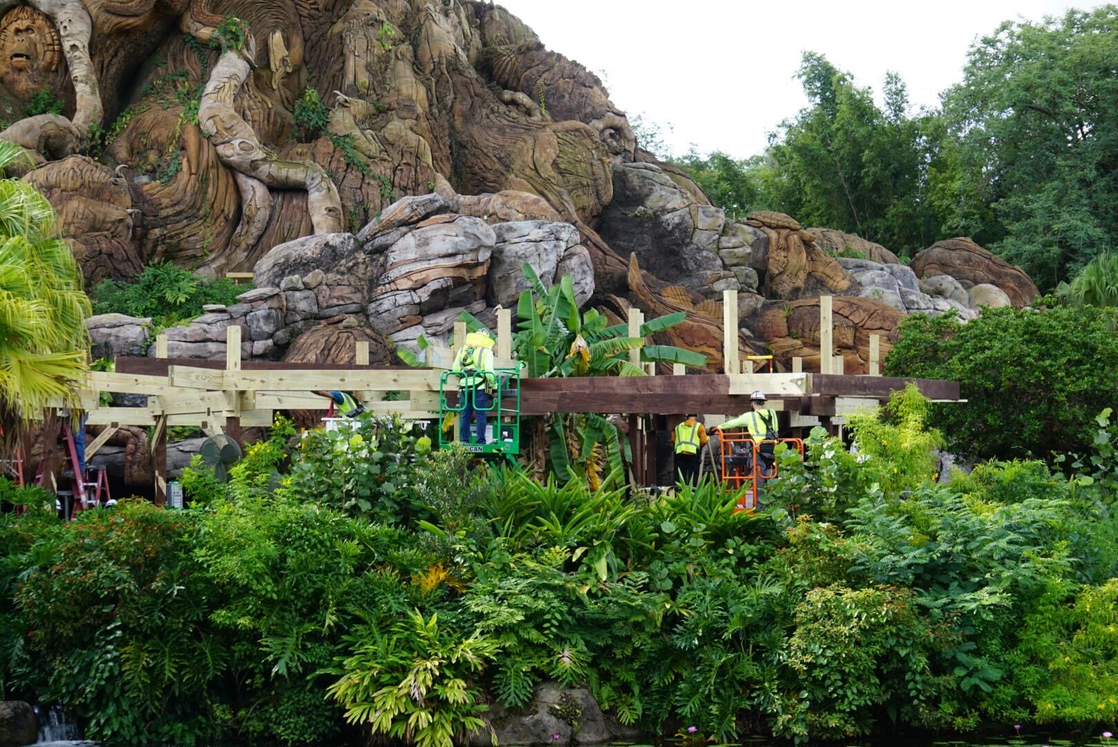 Construction workers build a wooden structure surrounded by lush greenery, capturing Animal Kingdom’s immersive Disney park style.