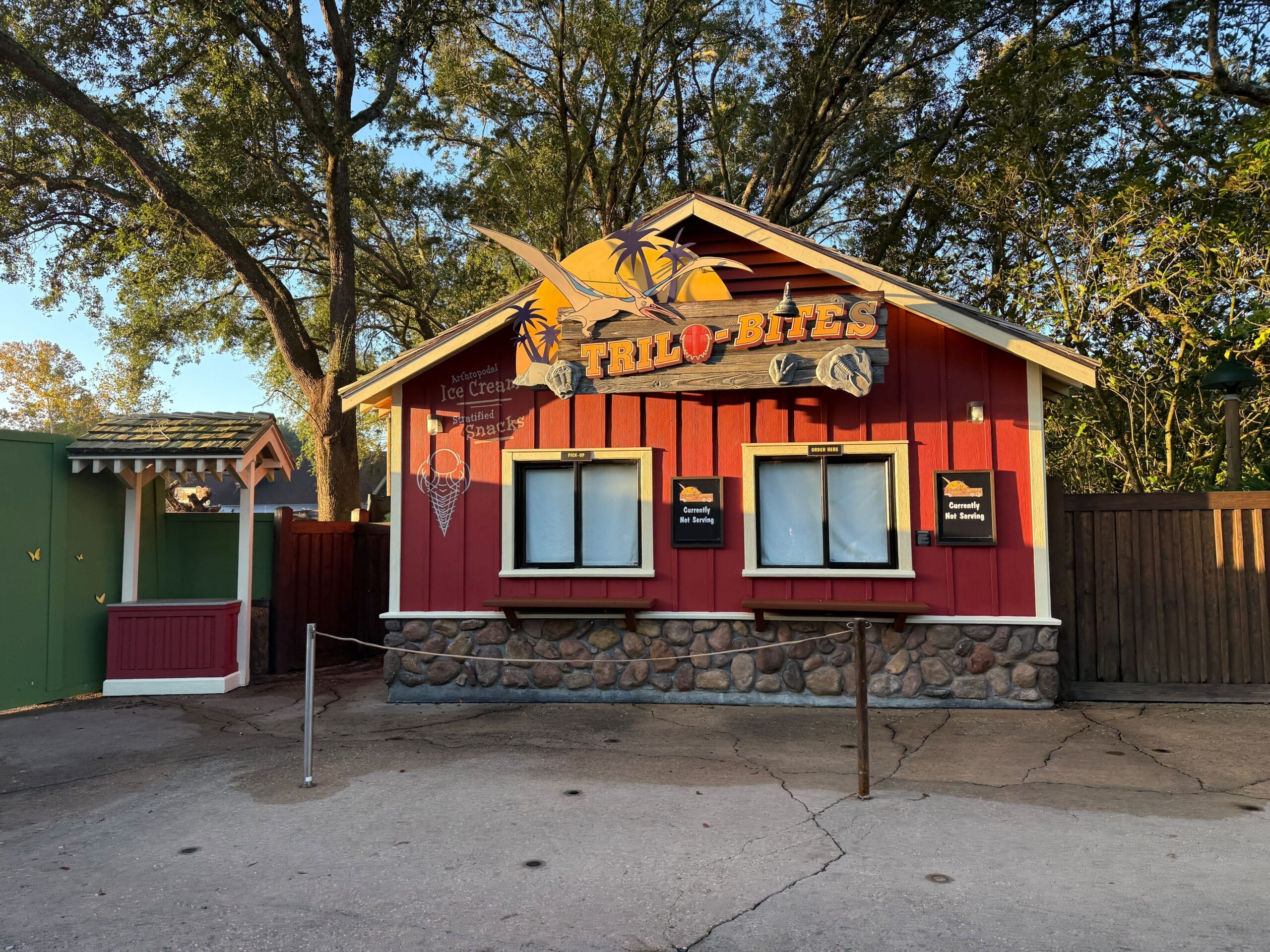 Trilo-Bites," a red food stand with stone details and closed windows, sits among trees—classic Disney World Dinoland ambiance.
