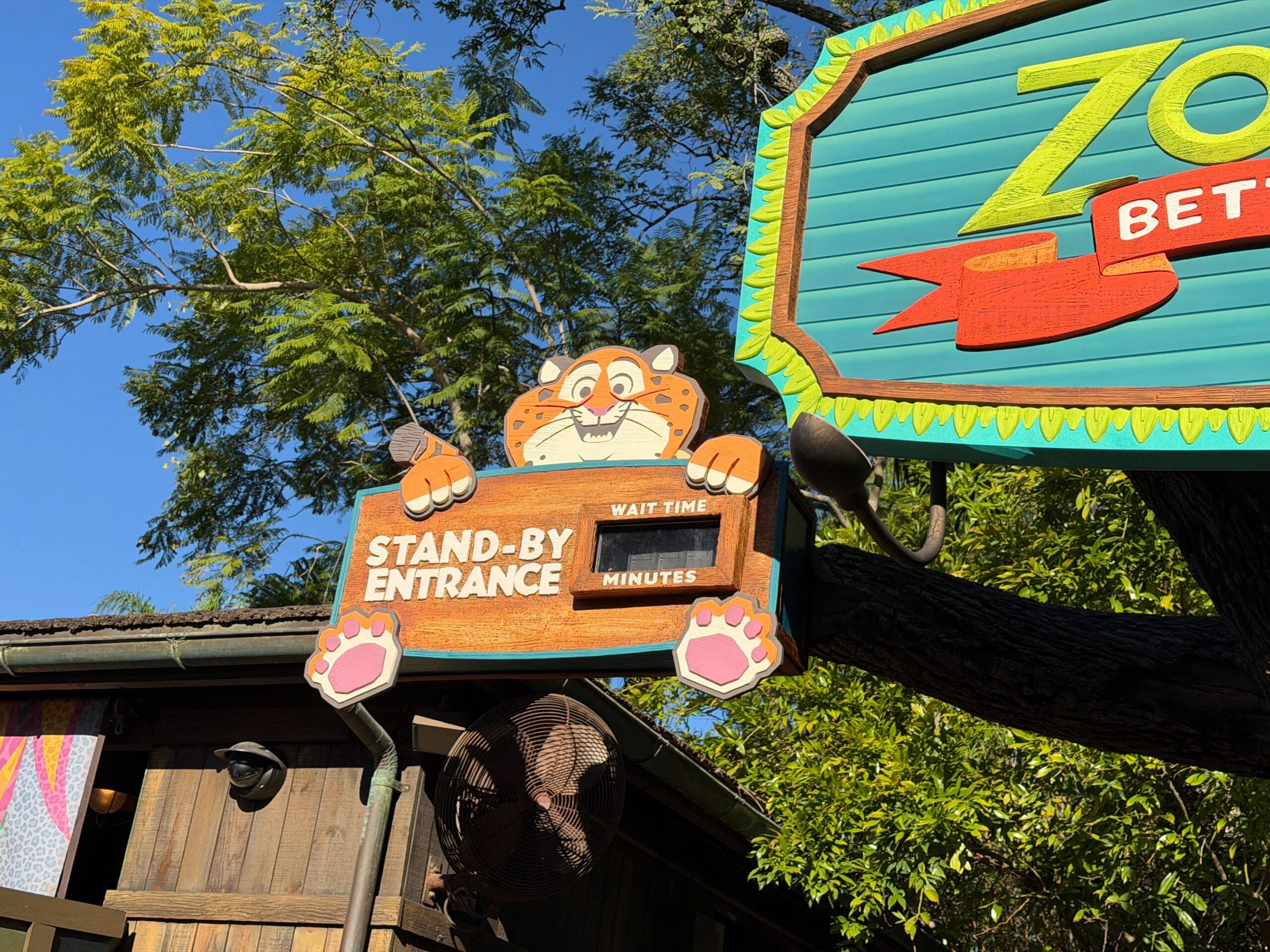 A cartoon tiger at Disney’s Animal Kingdom holds a "Stand-By Entrance" sign at a Zootopia attraction