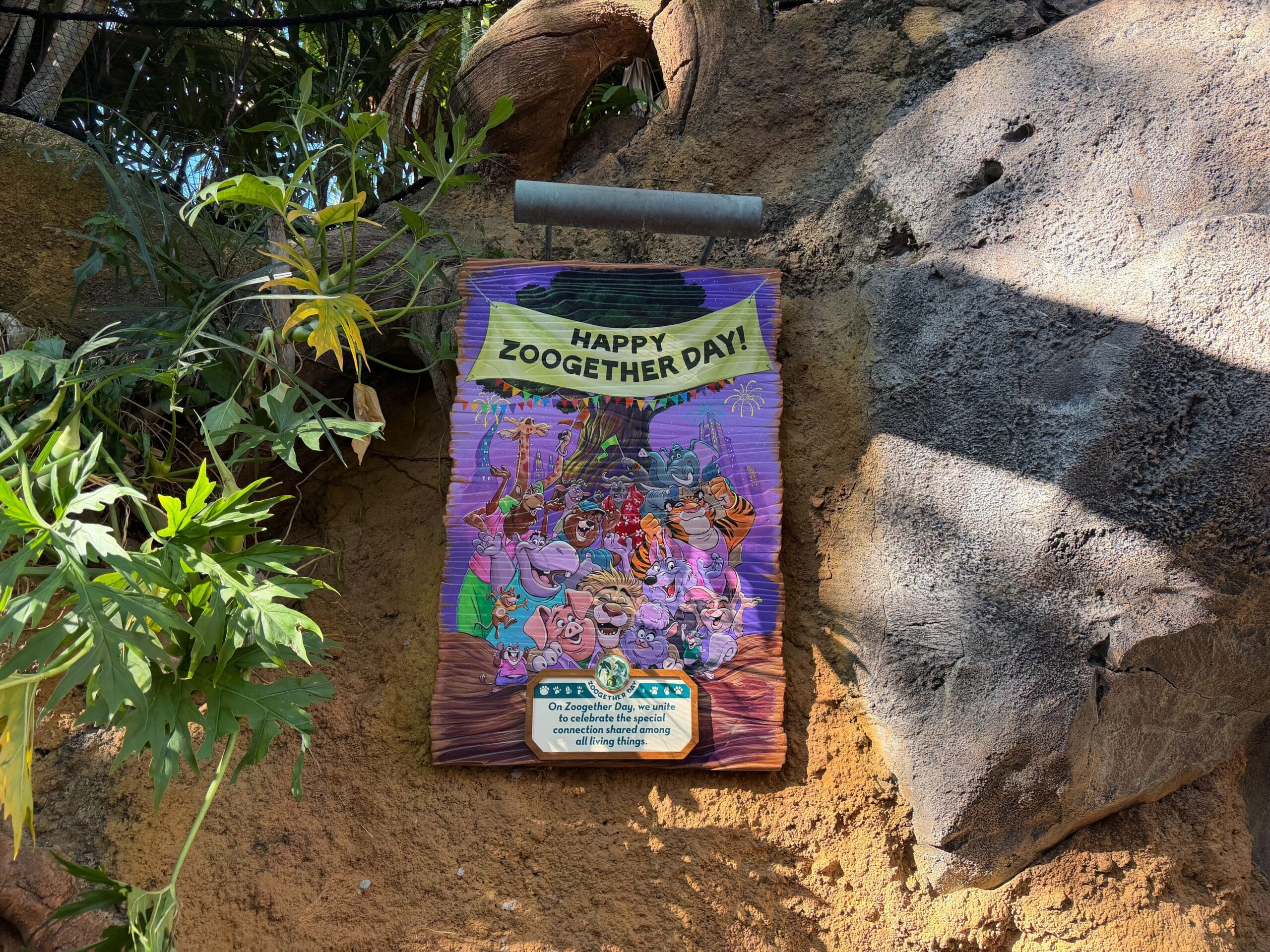 A festive sign on a stone wall says "Happy Zoogetger Day!" with cartoon animals partying, reminiscent of Disney park celebration decor.