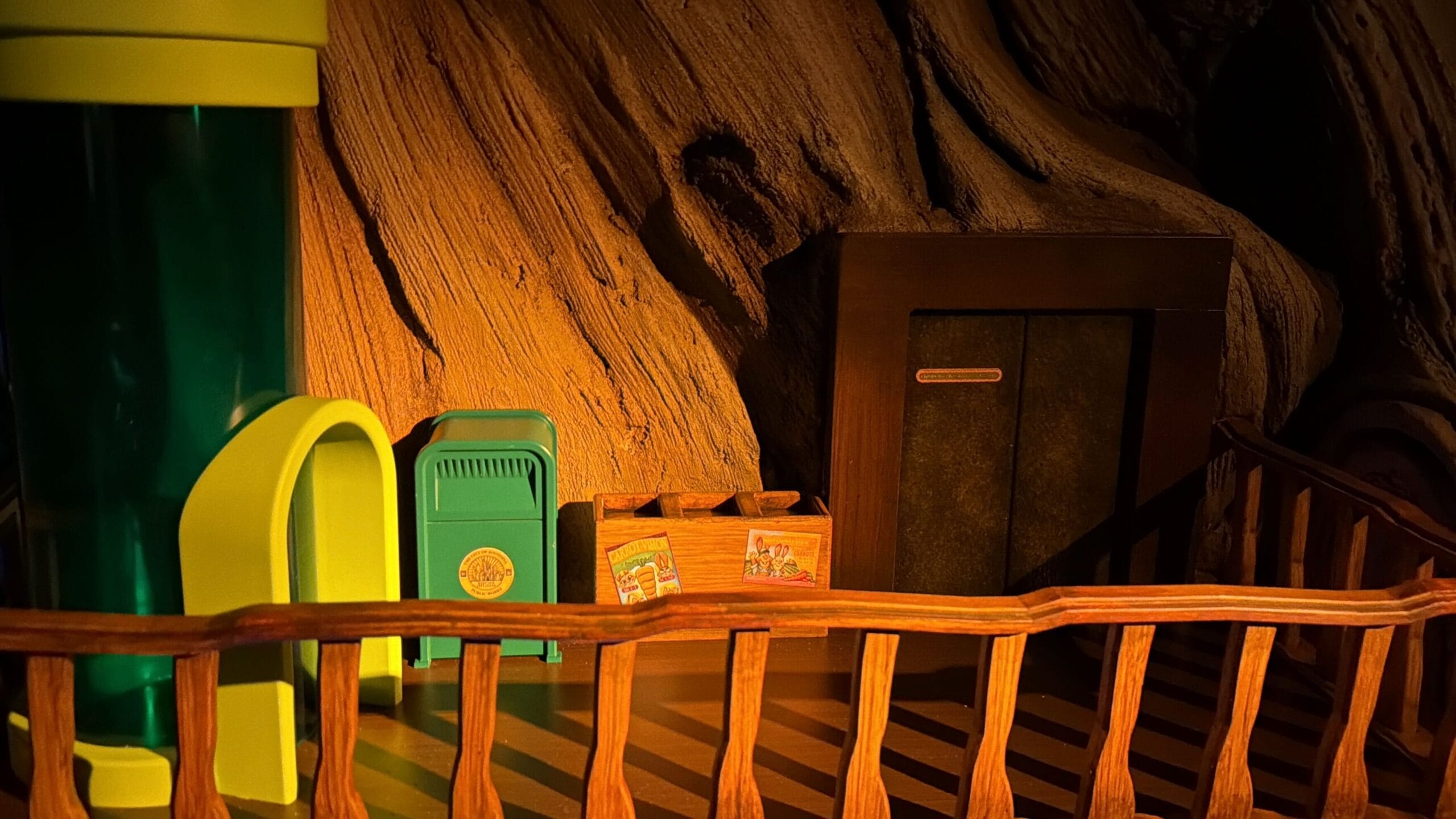 A whimsical wooden fence, green mailbox, and door on a tree-like wall with warm lighting, reminiscent of Disney park storytelling charm.