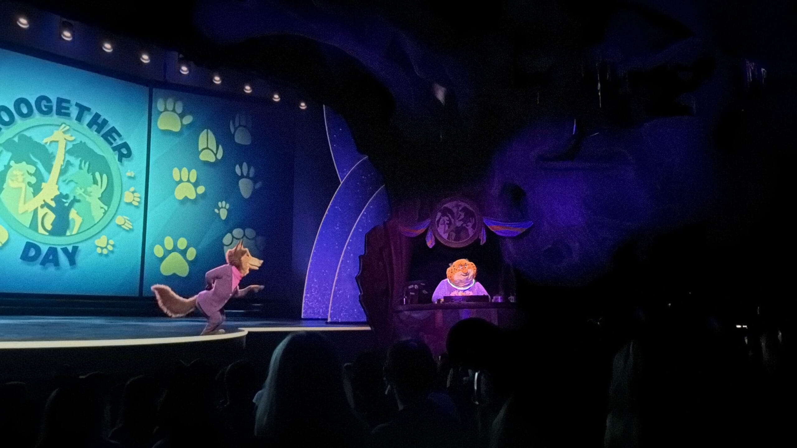Animated wolf performs on stage as tiger sits at desk during Zootopia Together Day in Disney’s Animal Kingdom theater.