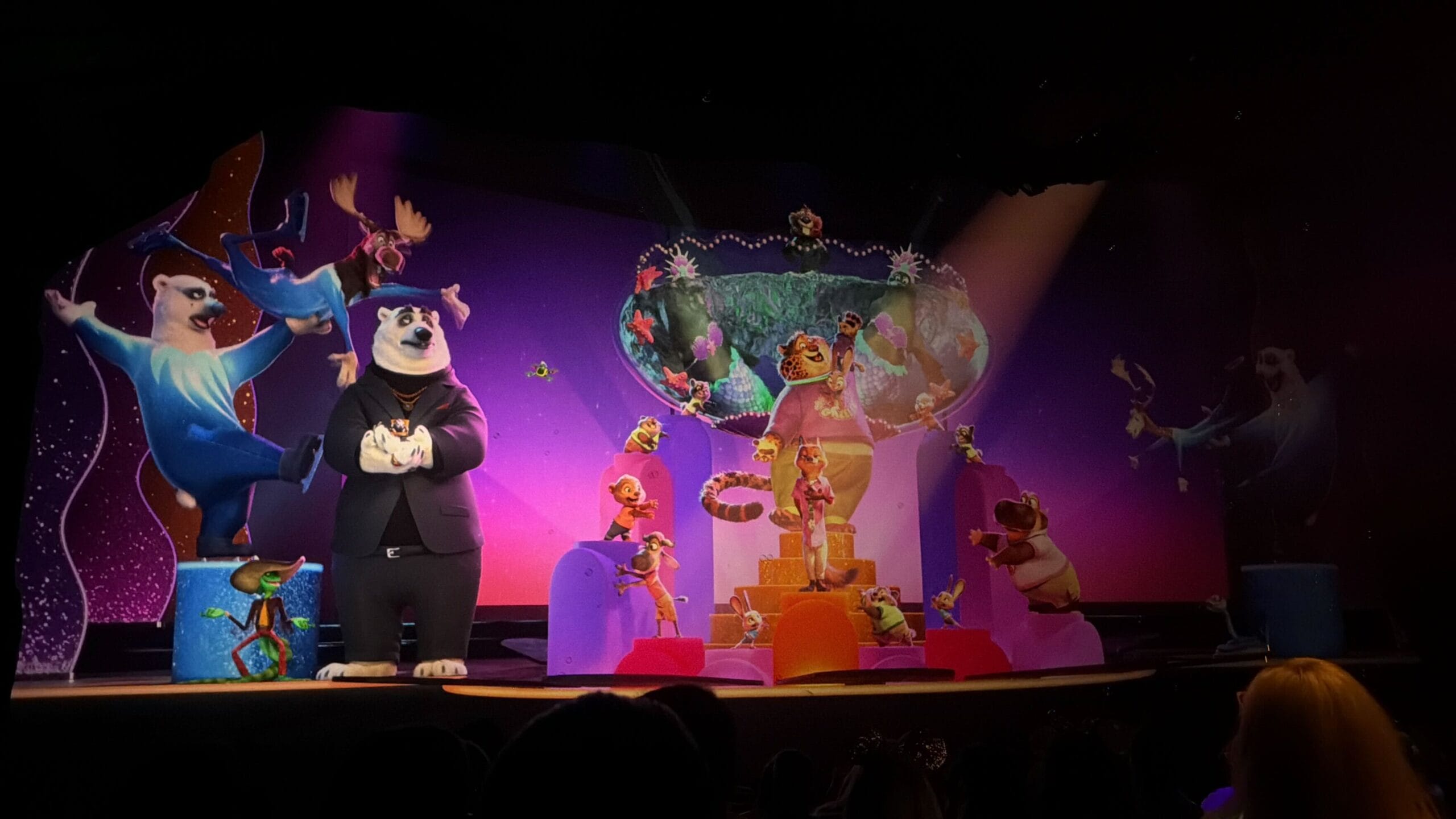 Costumed characters, including a tuxedoed polar bear, entertain on an Animal Kingdom-style stage at a Disney park.