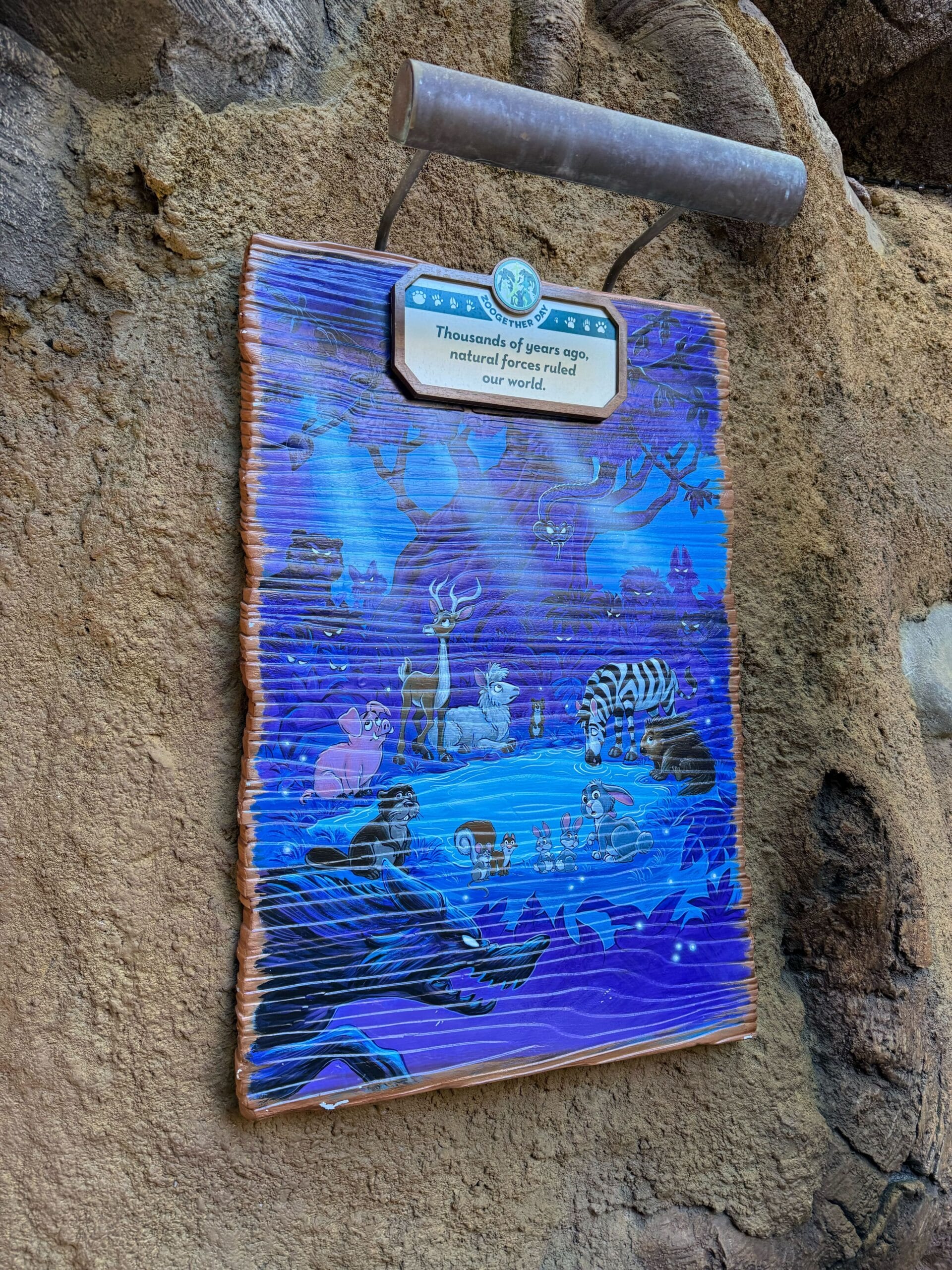 Vibrant Zootopia-themed sign on a stone wall, animals by water under stars, plaque overhead. No Disney castle in this scene.