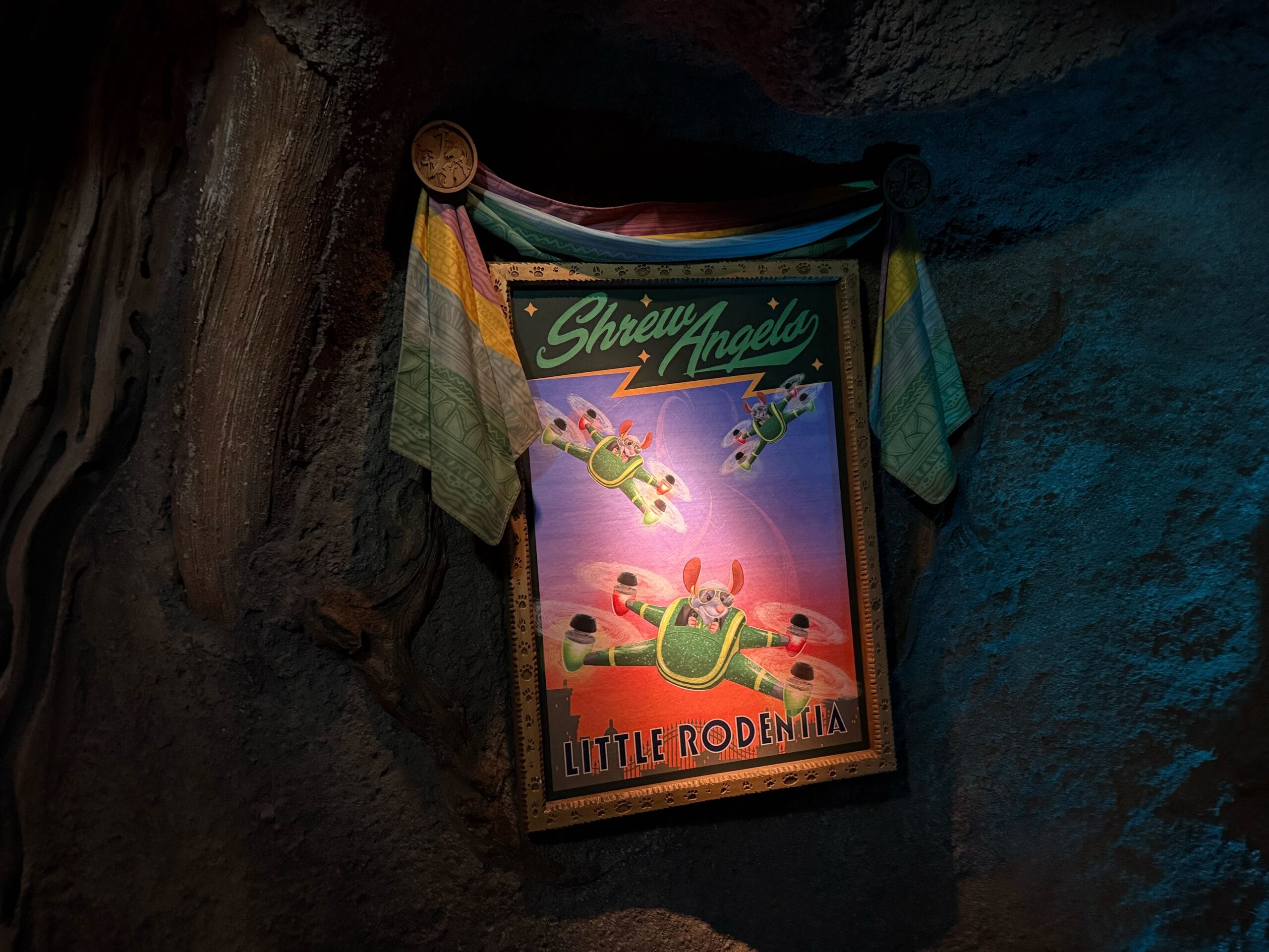 A Disneyland-style poster reads "Shrew Angels, Little Rodentia," with three cartoon mice flying green toy planes, cloth draped above.