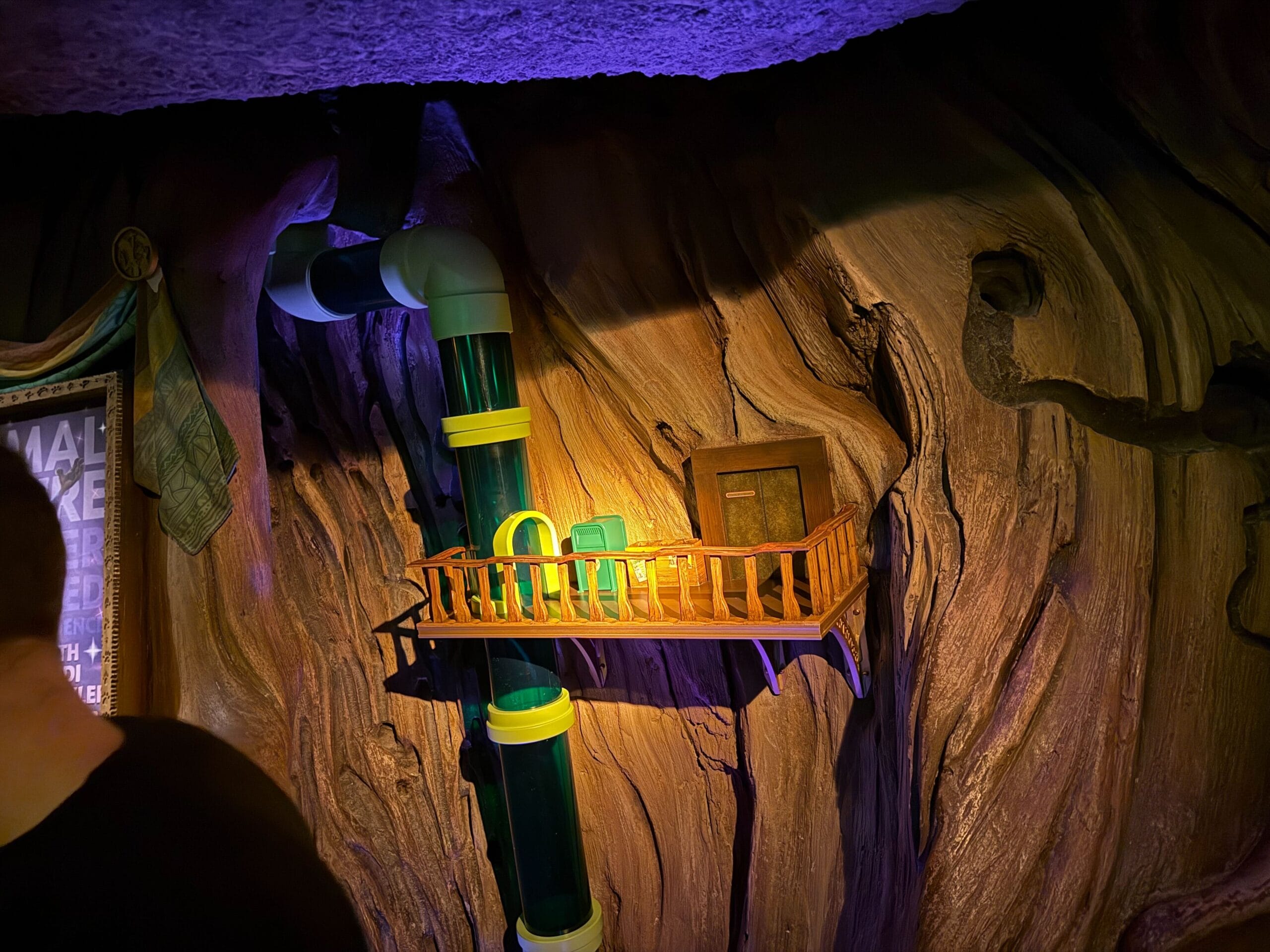 A cozy, Disney-style balcony with green pipes and a door on a whimsical, tree-like wall, glowing in warm yellow light.