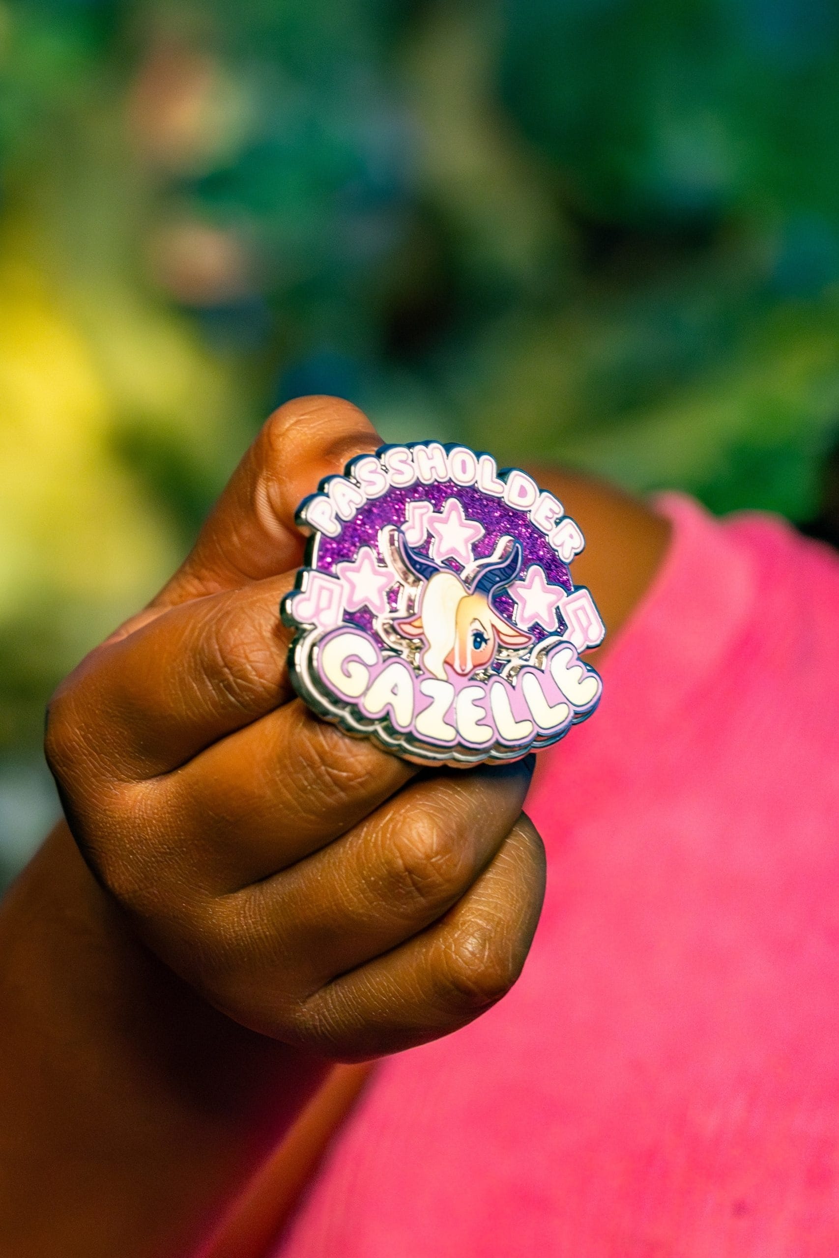 A hand displays a vibrant "Passholder Gazelle" pin featuring stars and a cartoon gazelle, a style often seen at Disney Parks.